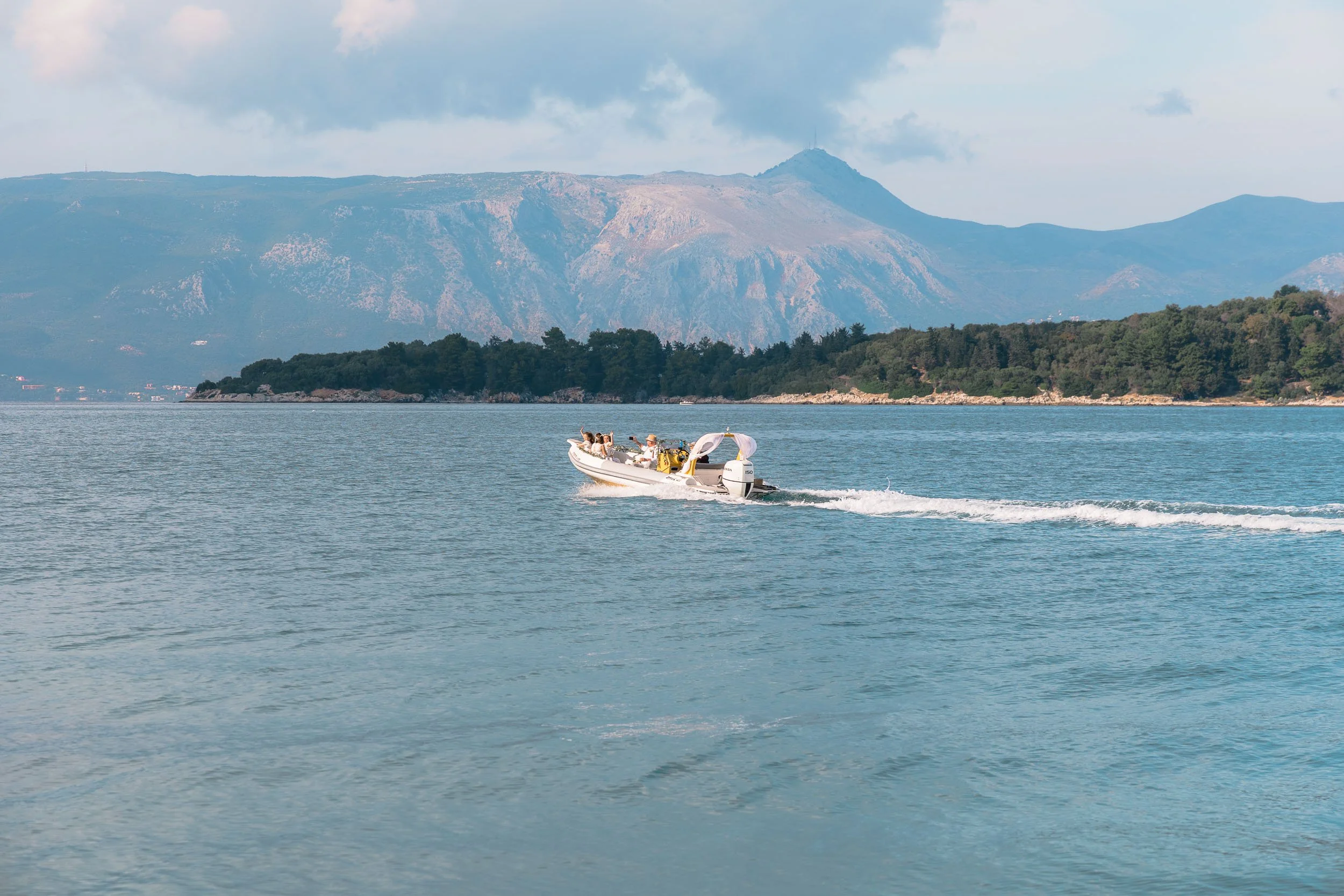 A white motorboat cruising on a body of water with mountains in the background and a partly cloudy sky.