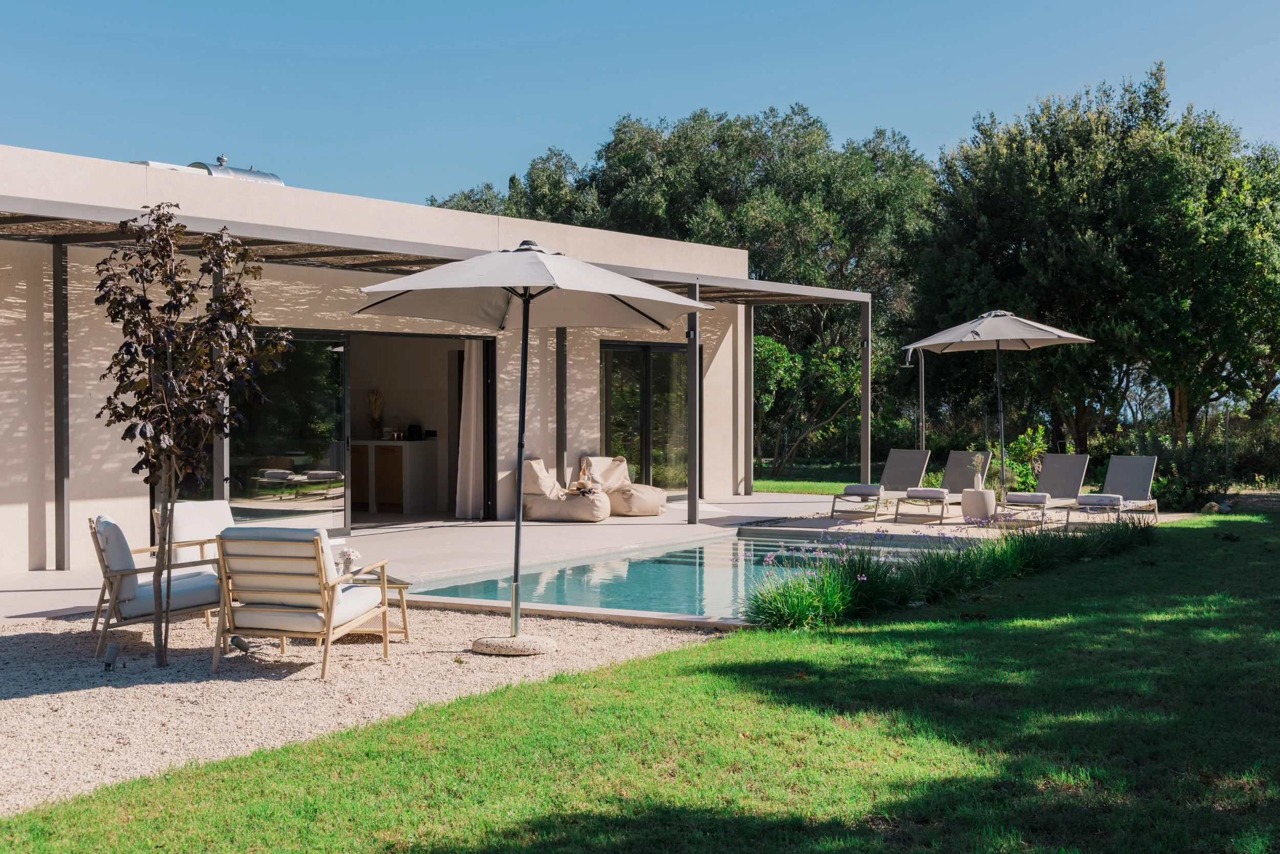 Modern house with outdoor pool, patio chairs, umbrellas, and lush green trees in the backyard