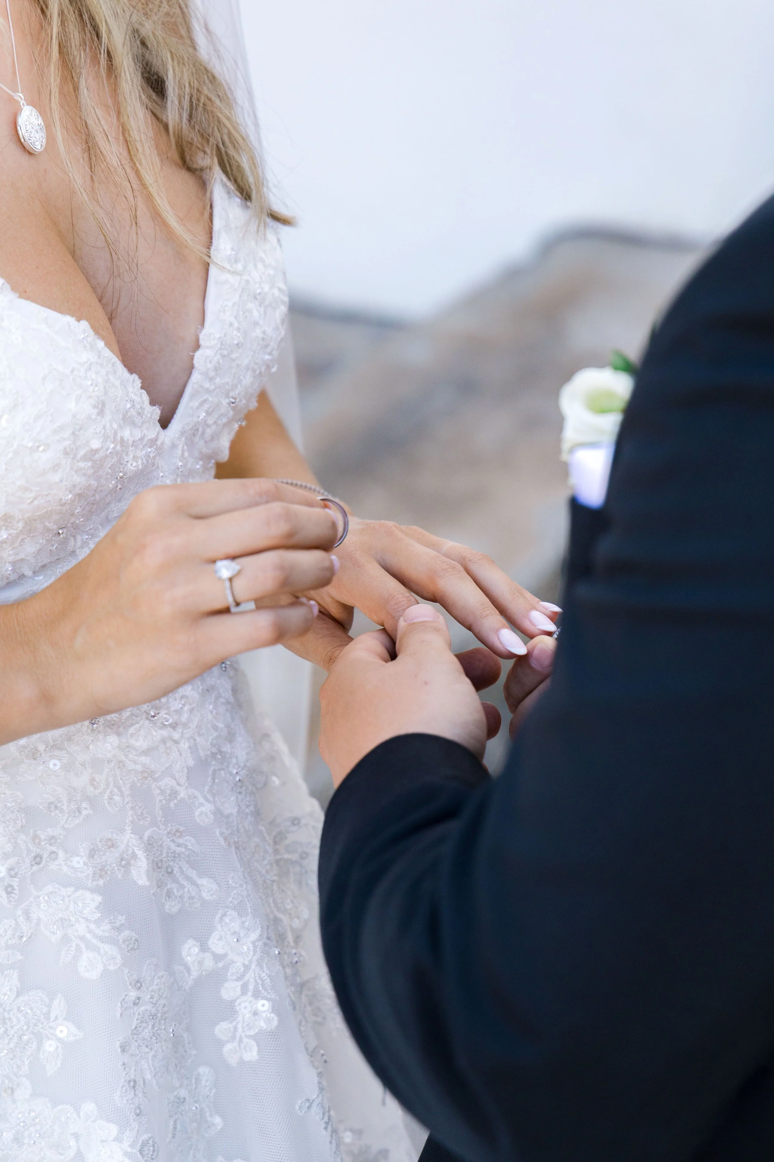 A bride and groom during a wedding ceremony, with the groom placing a ring on the bride's finger.
