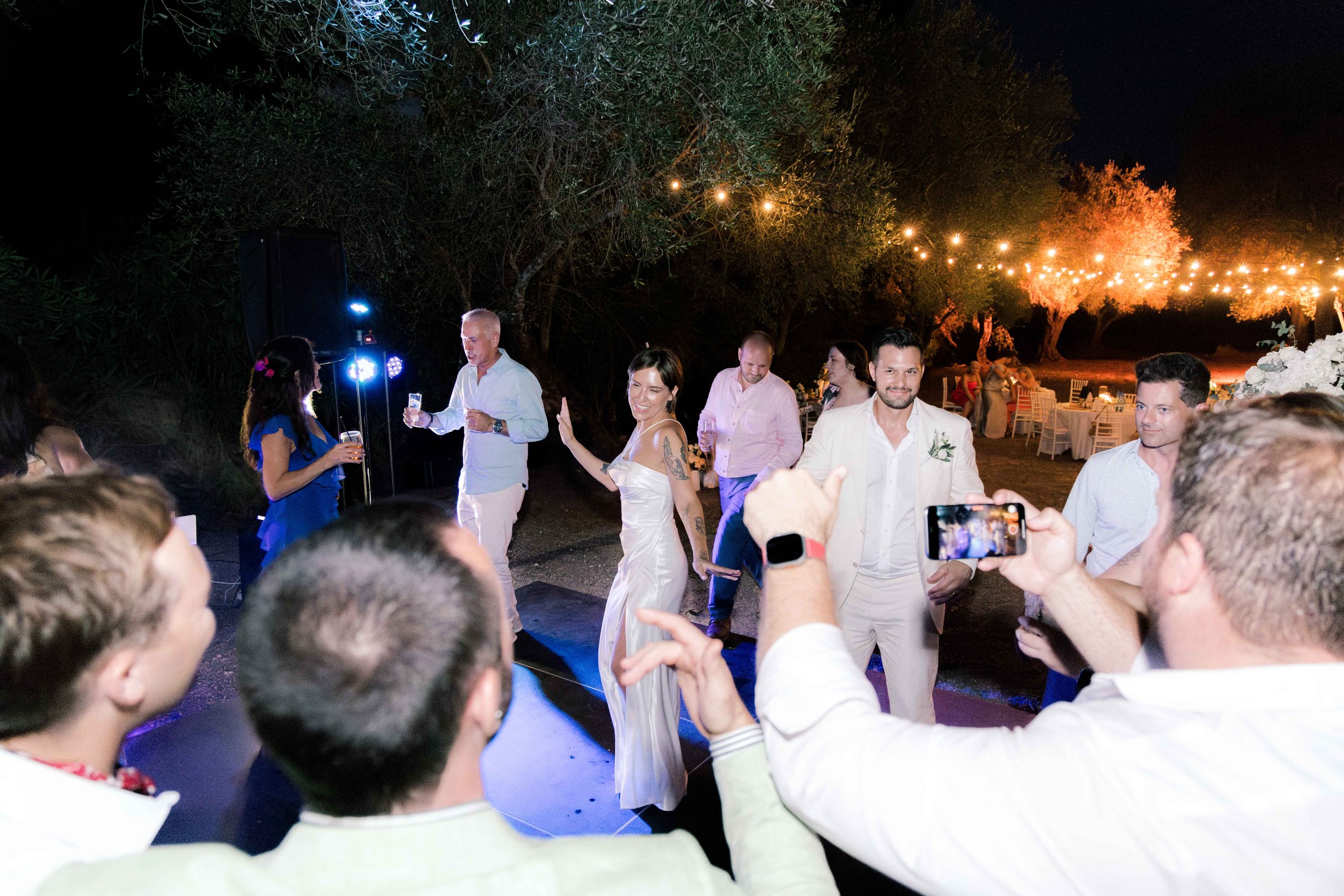 People at an outdoor wedding reception dancing and celebrating under string lights at night.