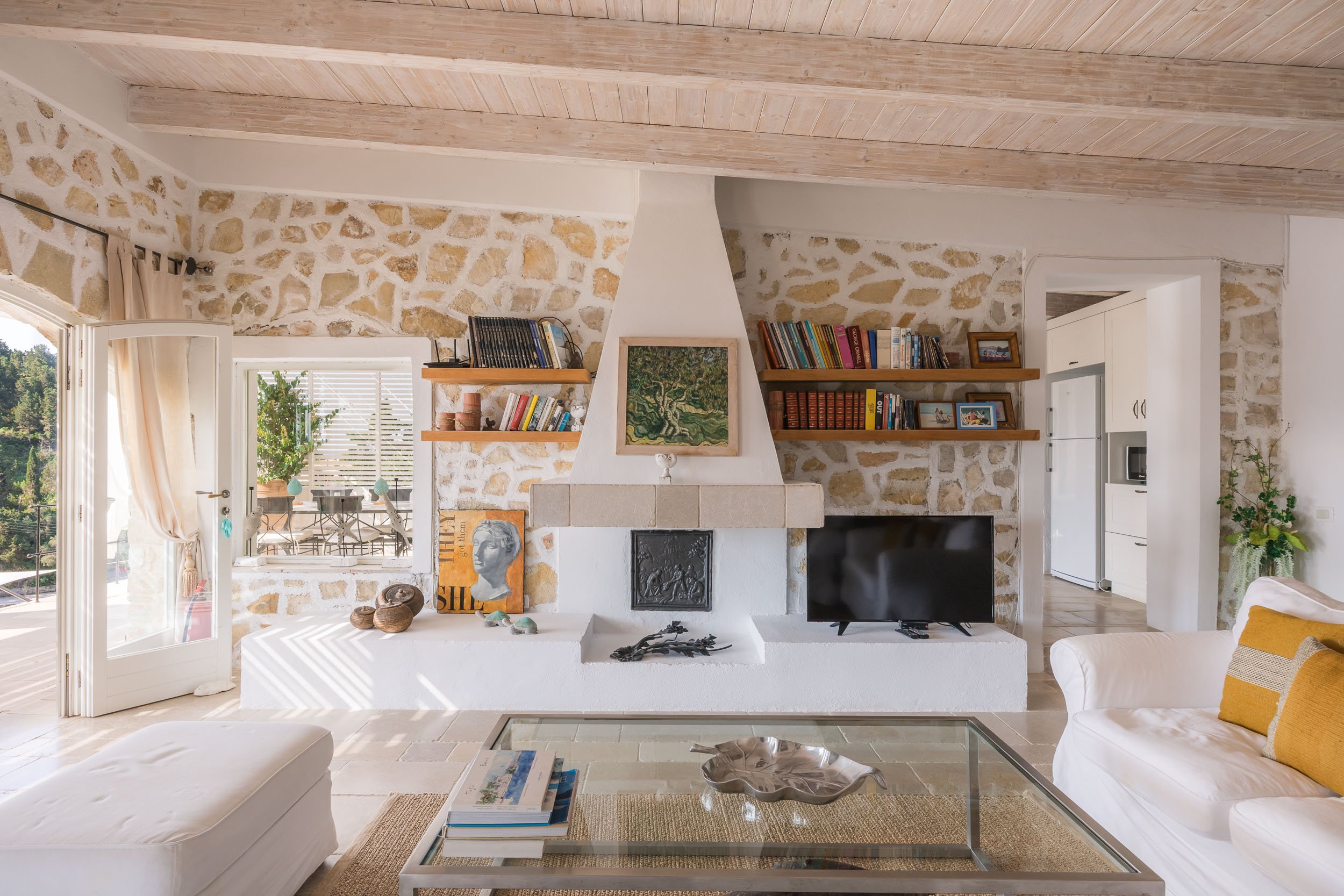 Bright living room with stone walls, a fireplace, bookshelf, and sliding glass door leading to a balcony with outdoor seating.