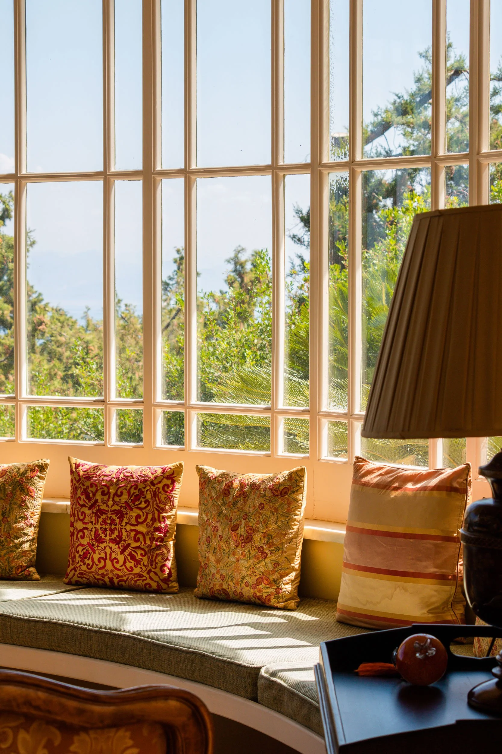 Sunlit window seat with colorful decorative pillows and lush greenery outside.