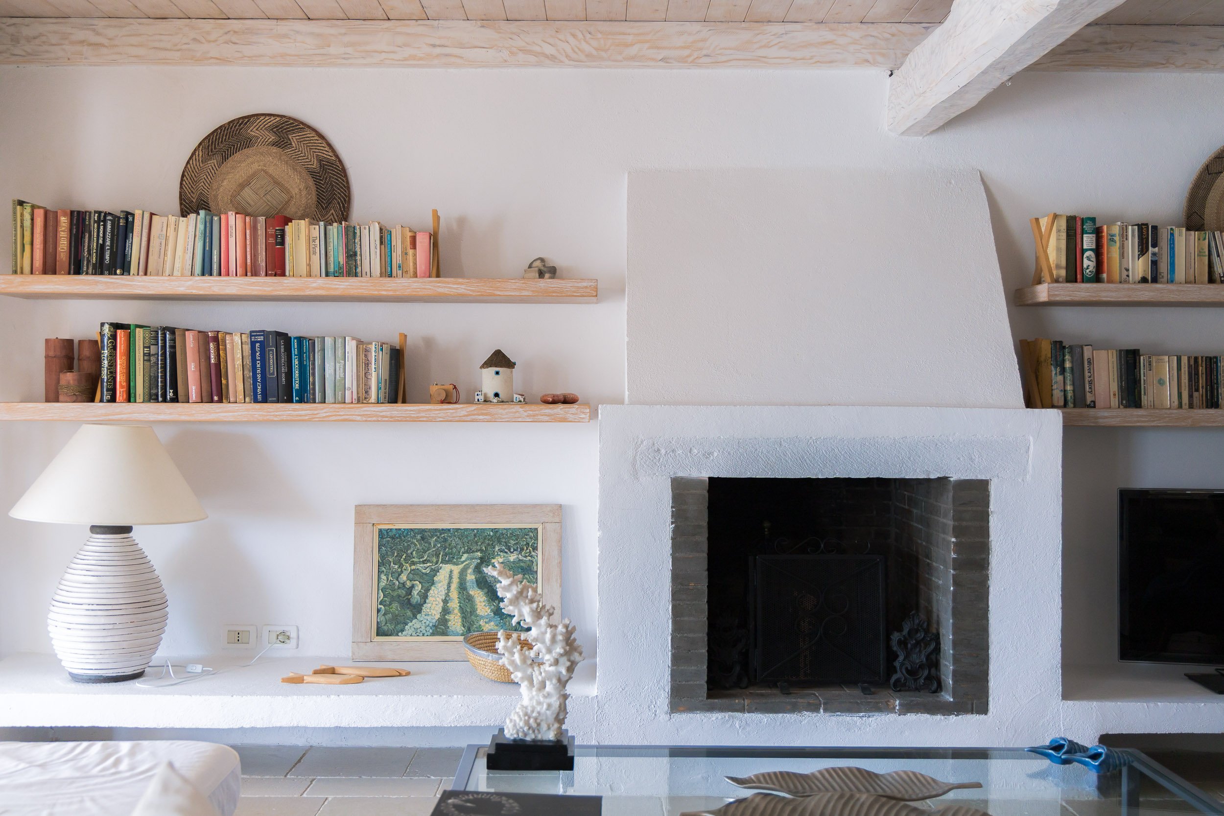 Living room featuring a white fireplace, wooden shelves with books, a table lamp, a framed painting, and decorative items.