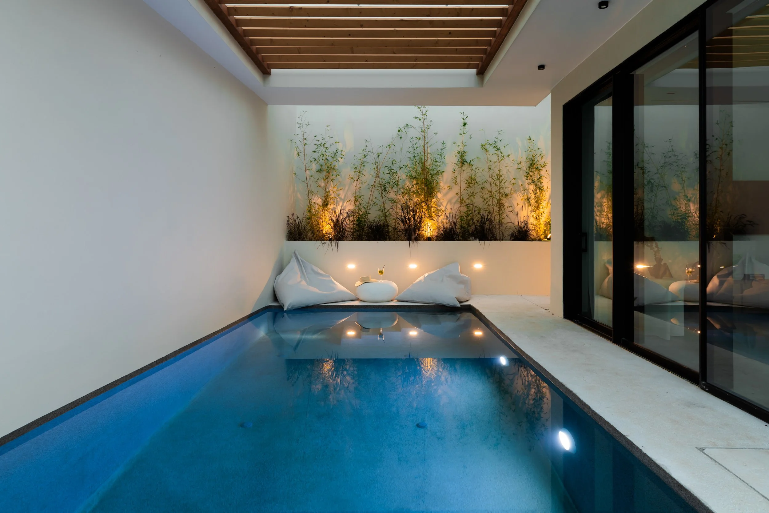 Indoor swimming pool area with a small pool, white pillows, and a decorative wall with plants and warm lighting.