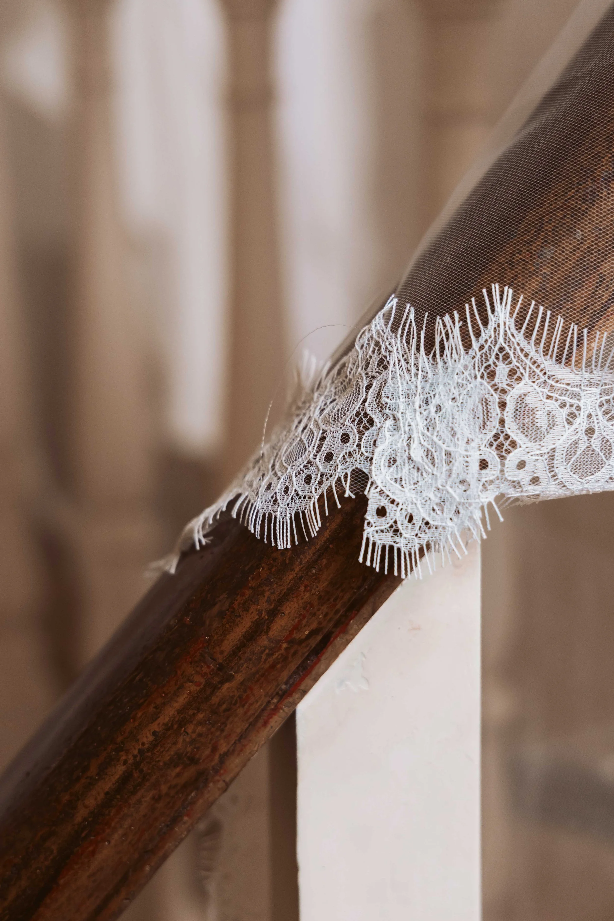 Close-up of a wooden stair railing with white lace fabric draped over it.