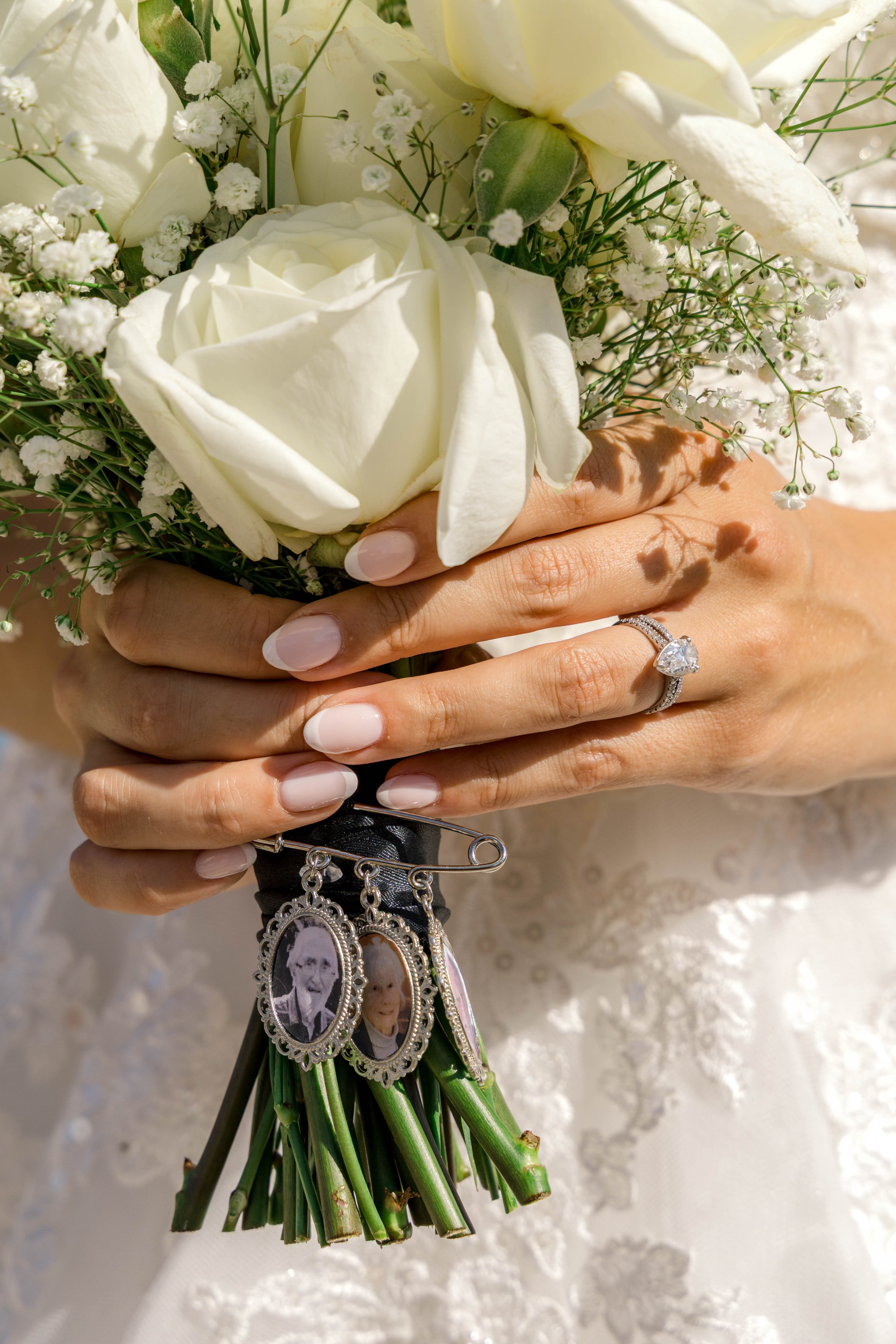 Close-up of a bride's hands holding a bouquet of white roses and baby's breath, with her wedding ring visible.
