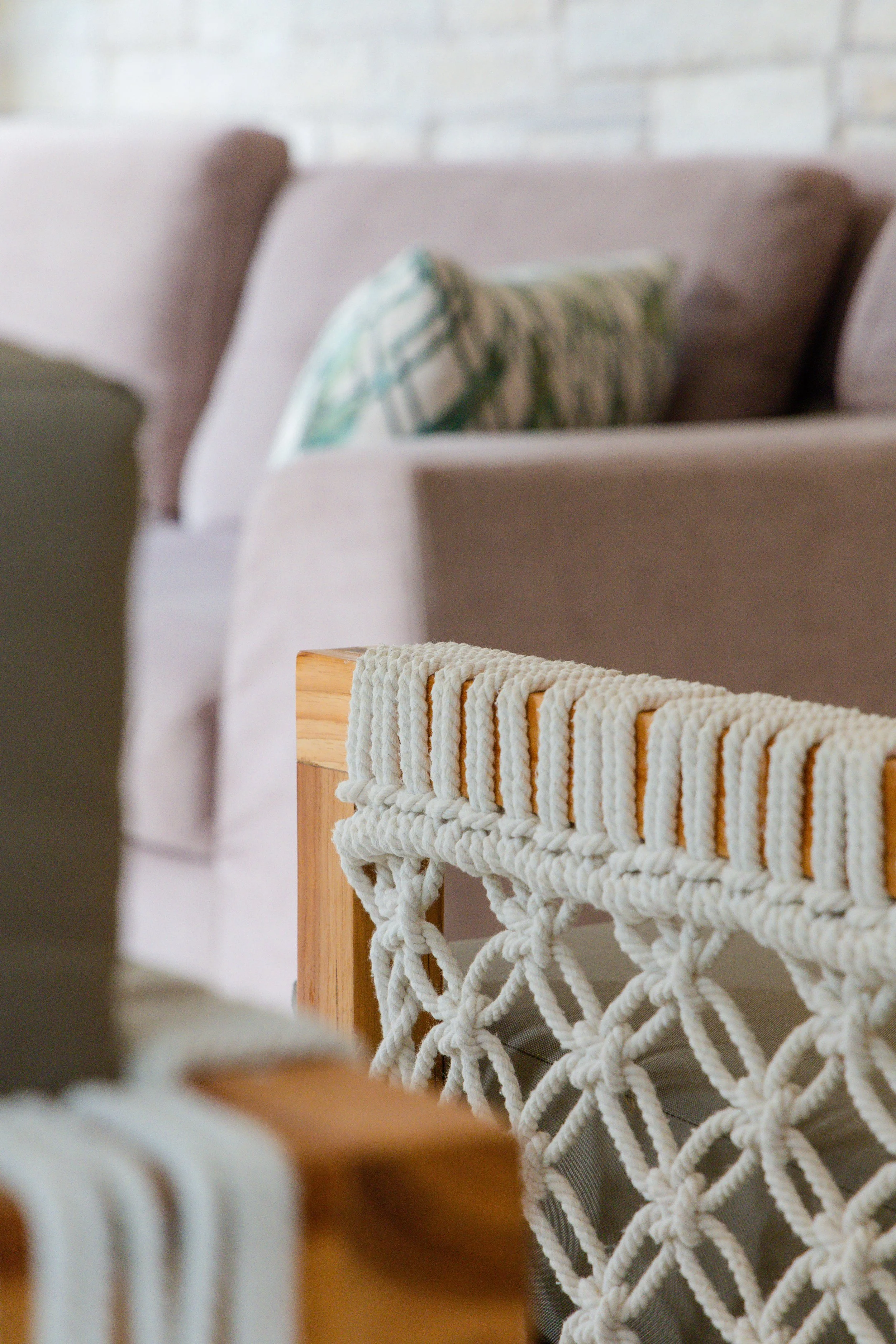 Close-up of a wooden furniture piece with a decorative woven rope design, against a background of beige sofas with patterned cushions.