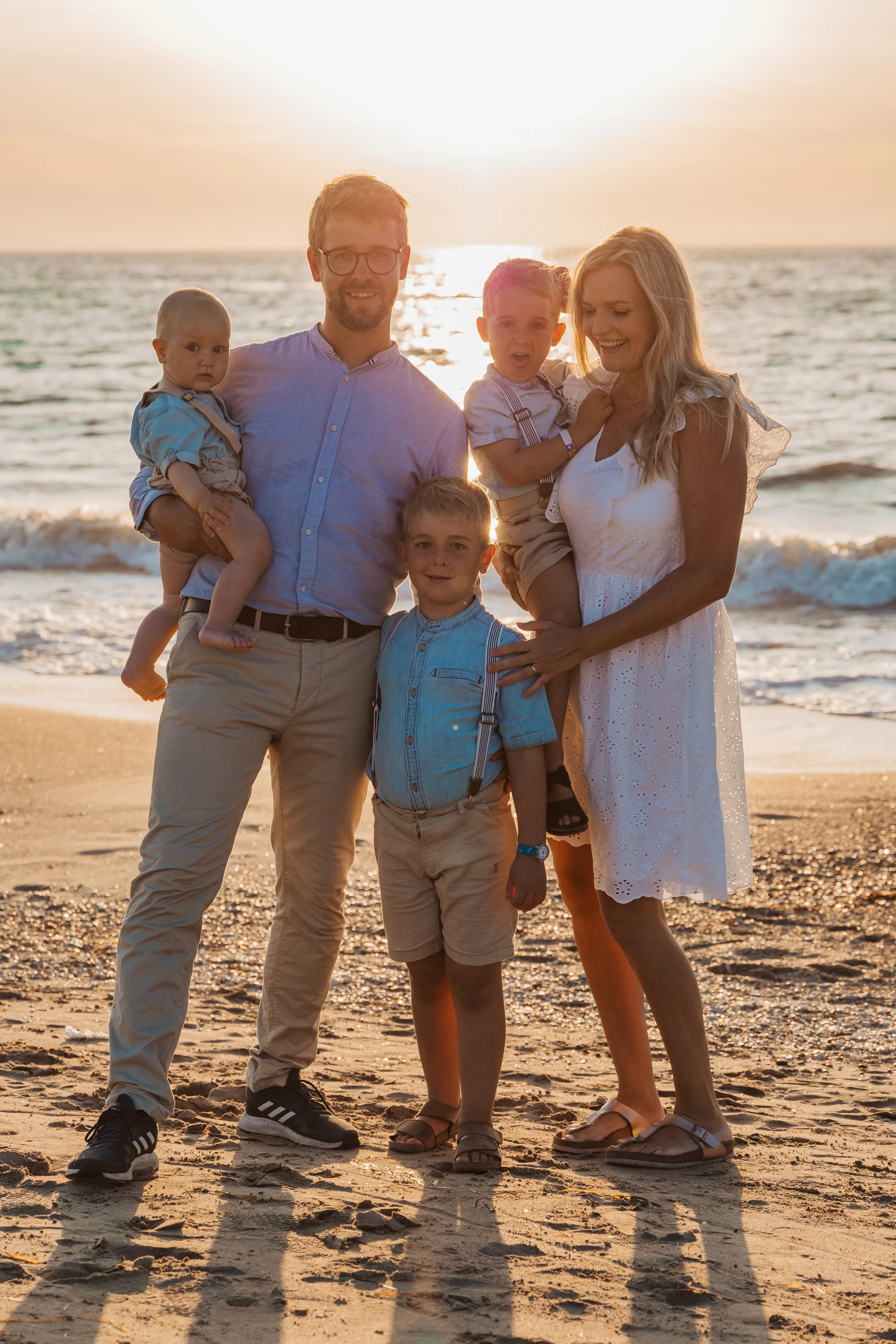 Family of six at the beach during sunset, with children and parents smiling.
