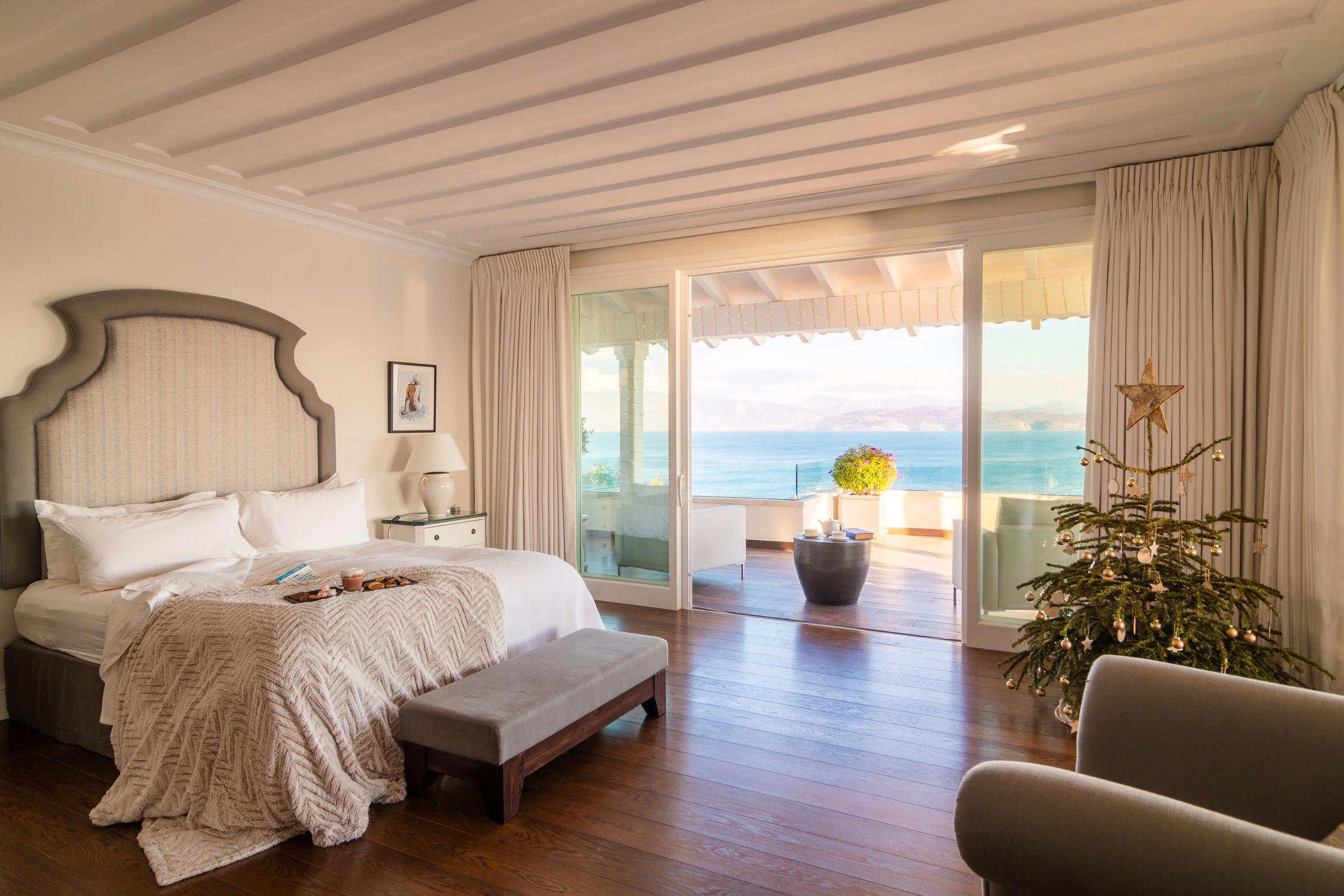 A bedroom with a view of the ocean, decorated for Christmas with a small Christmas tree.