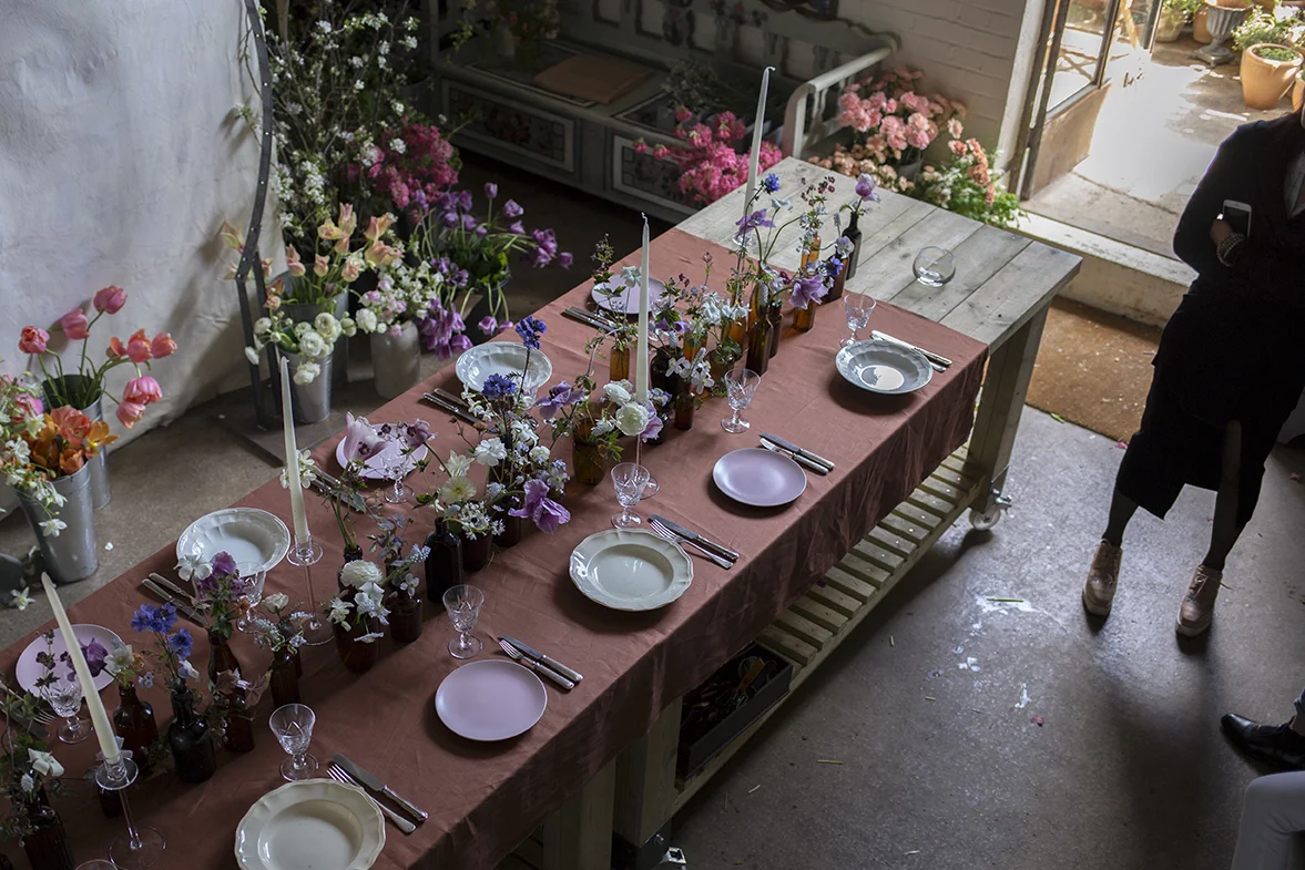 A richly coloured combination of white, lilac, blue and purple flowers arranged in amber glass medicine bottles for a sumptuous spring tablescape.