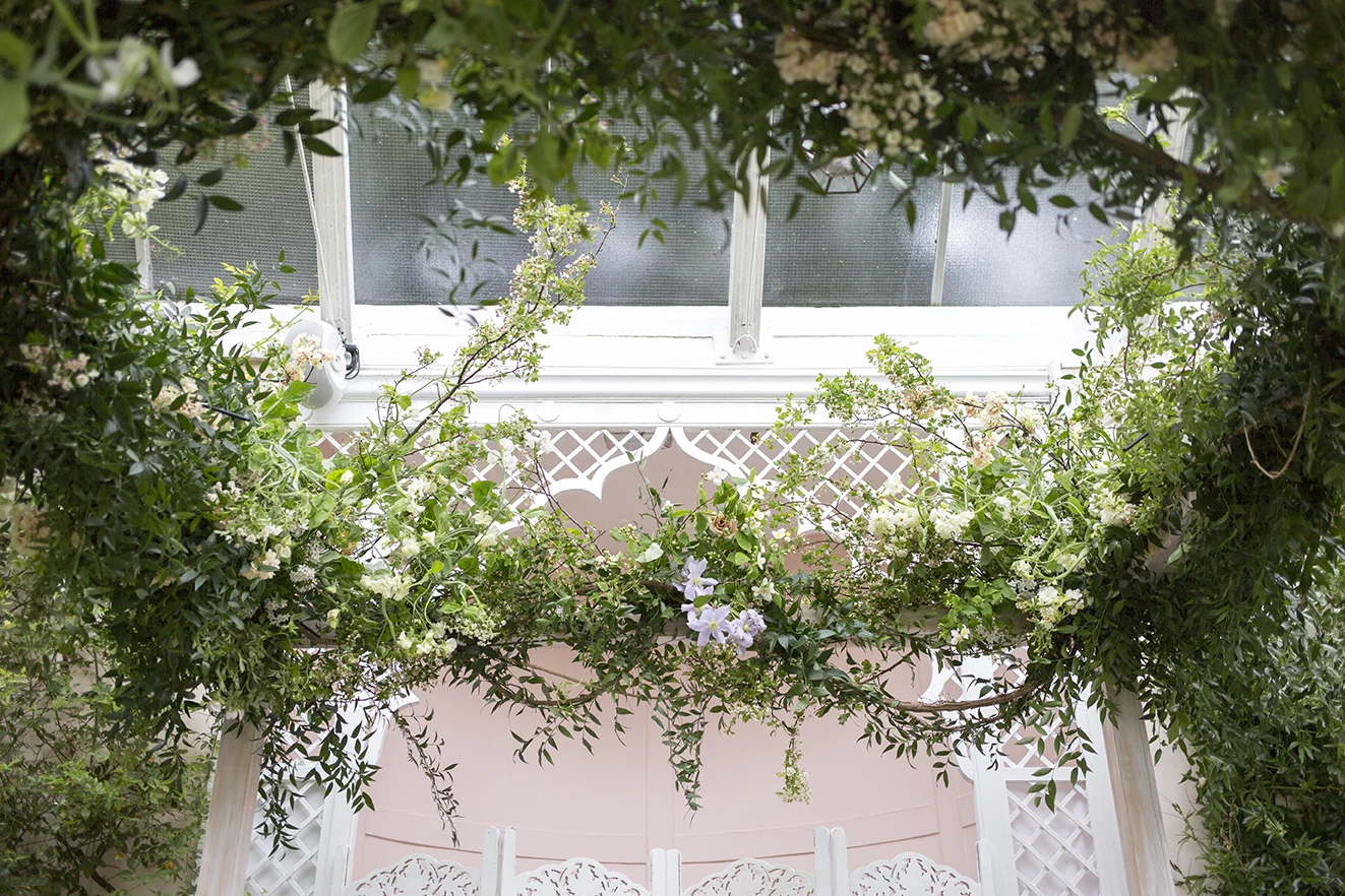 Installation | The chuppah, dressed with clematis vines, hawthorn, spring blossom, sweet pea and potato vines, and garden roses, for David and Tash’s wedding ceremony, in the ornate curved Orangery at Sezincote House