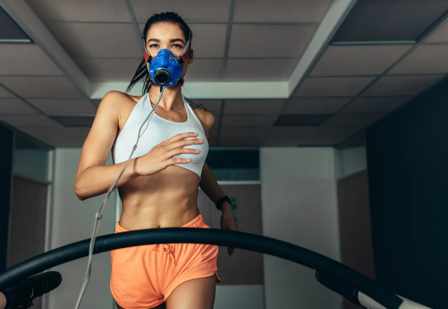 image of a woman running on a treadmill with a VO2 max mask monitor on her face.
