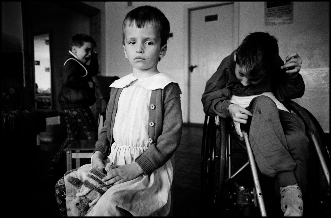  BELARUS. 1997. Novinki Asylum, Minsk. A hydrosyhalic child surrounded by the chaos of the asylum.  