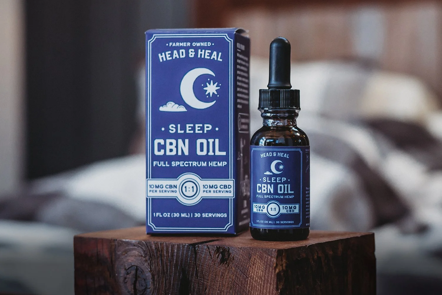 A 1 fl oz (30 ml) bottle and box of Head & Heal Sleep CBN Oil on a wooden block. The blue packaging features a moon and star icon and states it contains 10 mg of CBN and 10 mg of CBD per serving
