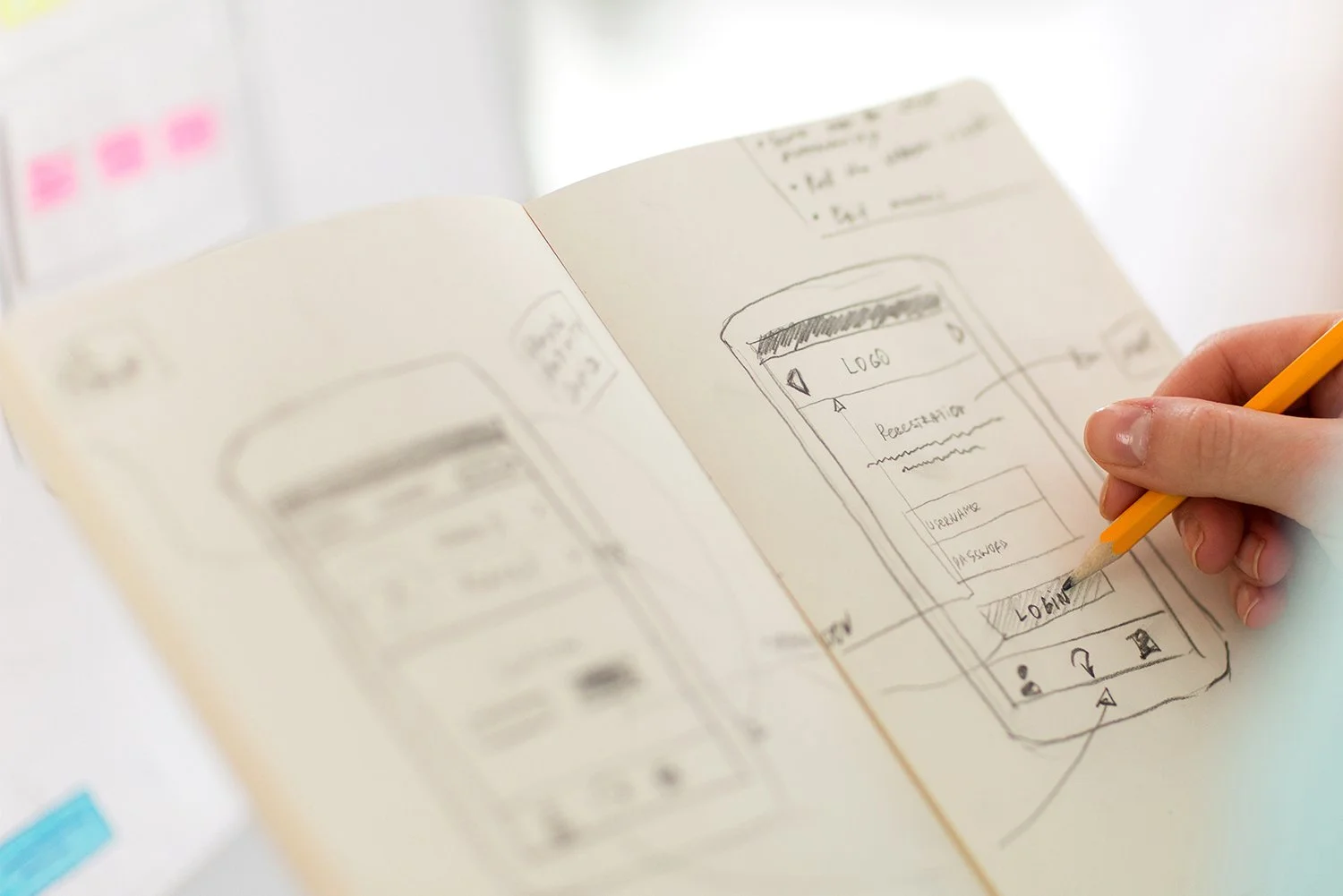 A UI designer sketching a mobile application wireframe in a notebook using a yellow pencil, showing a detailed login screen design