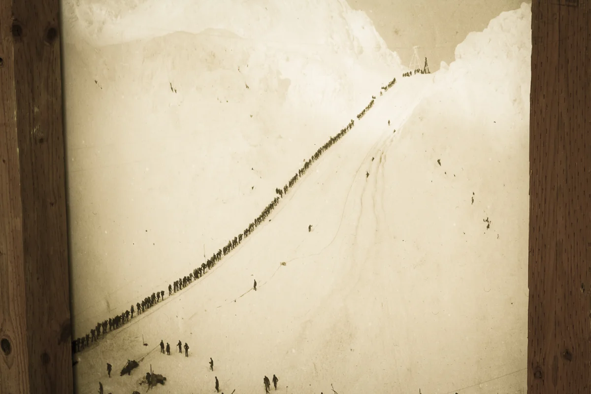 An old photo of men queuing through a pass on the Chilkoot Trail.
