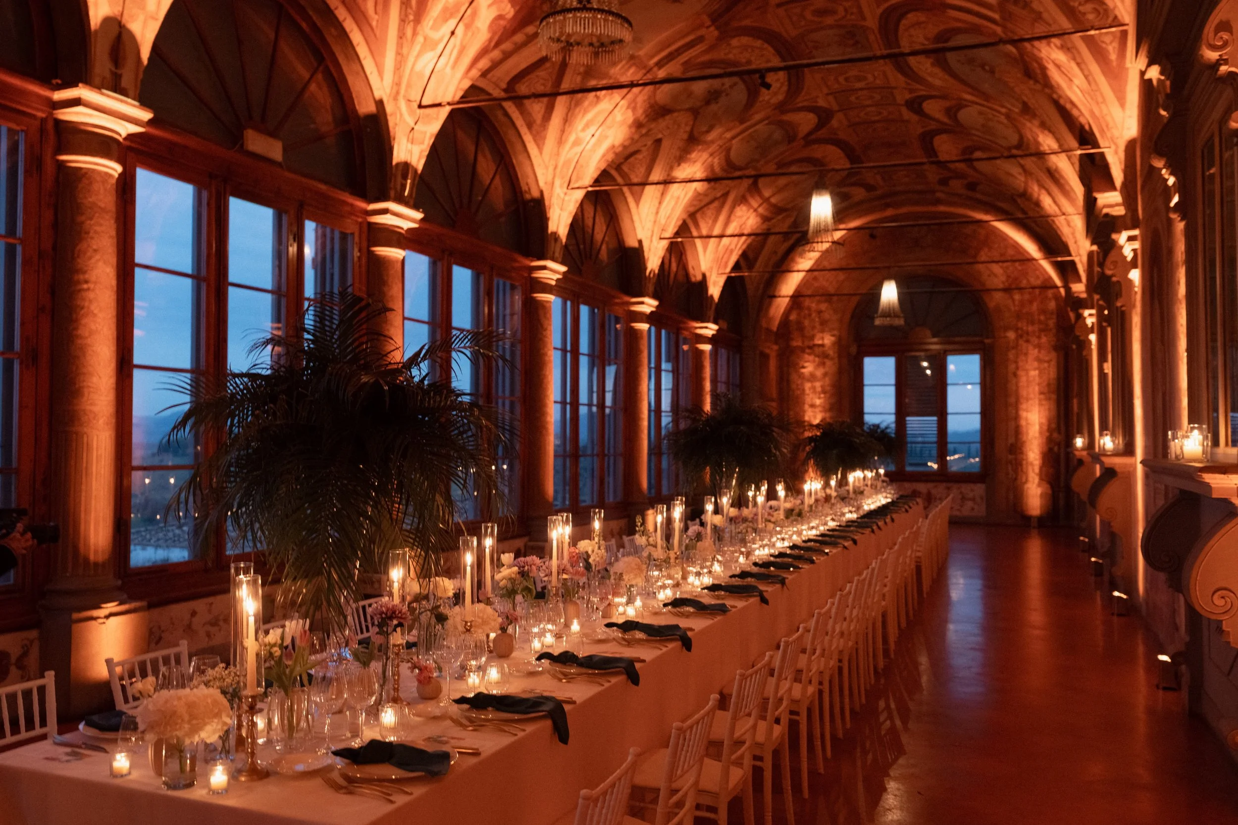 Candlelit banquet table with palm trees inside the frescoed loggia gallery of Villa Corsini a Mezzomonte.