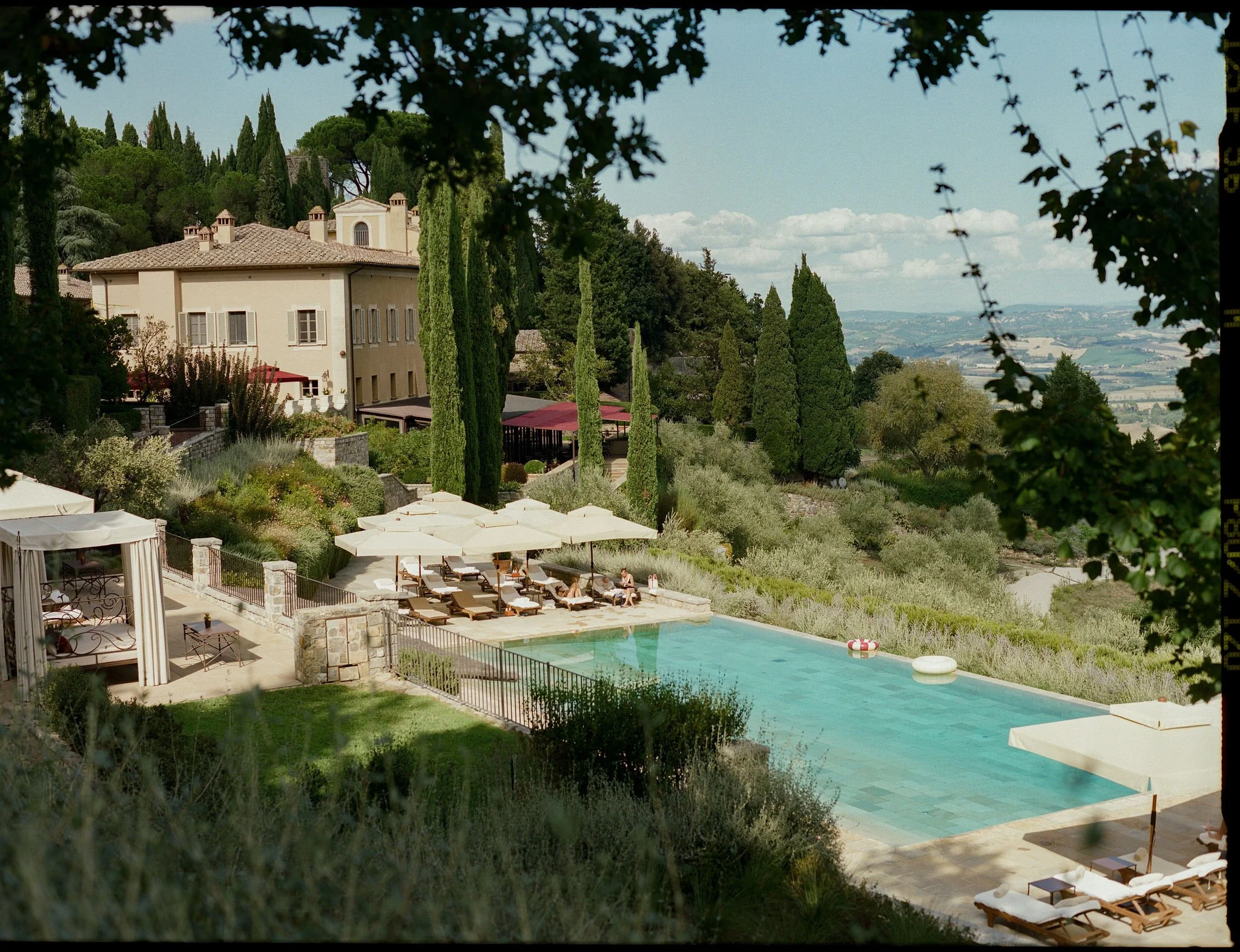 Luxury private Tuscan villa estate with an outdoor swimming pool, sun loungers, and panoramic views of cypress trees and rolling hills.