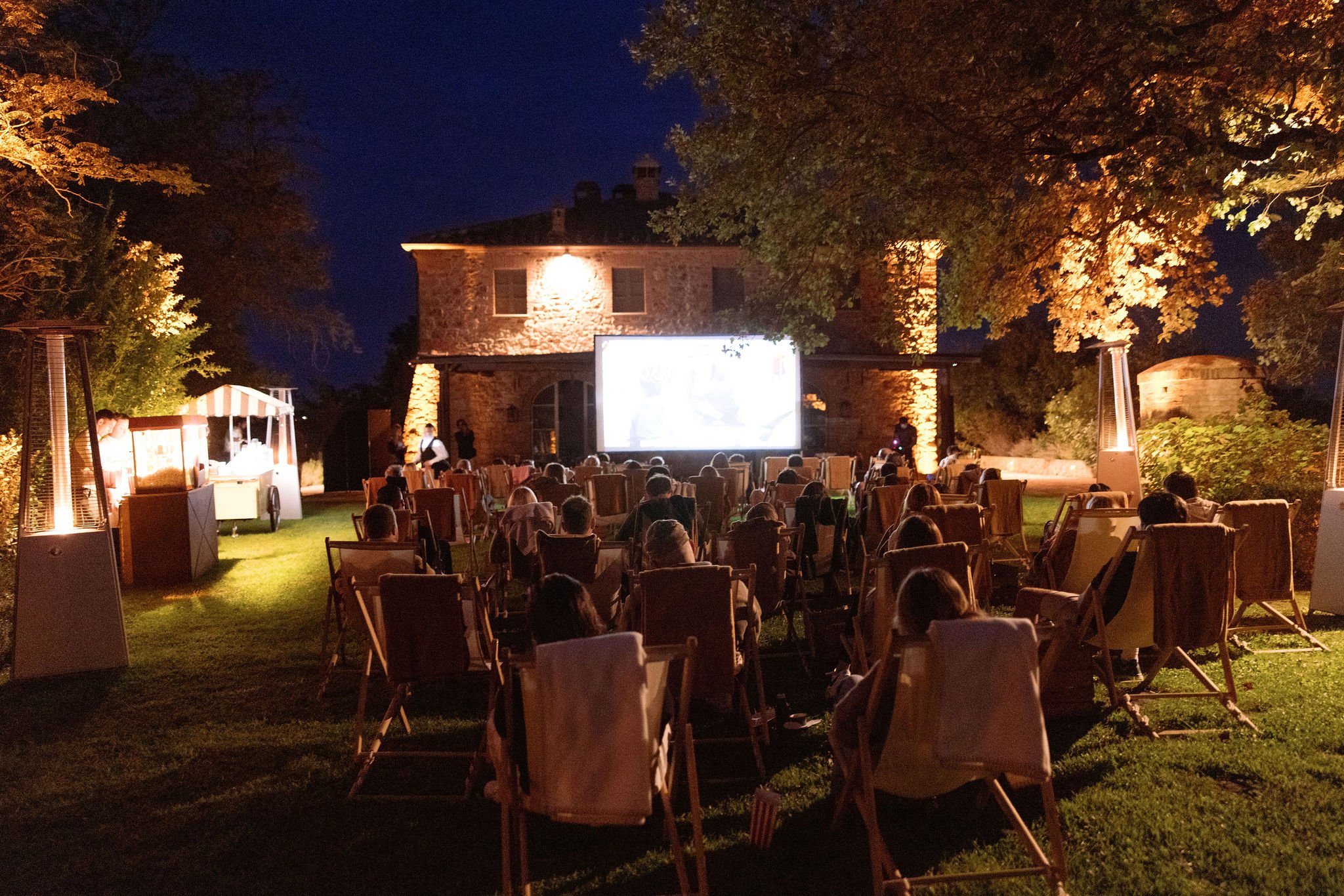 Movie night in a countryside villa with 60 guests comfortably sitting in low chairs with blankets. Popcorns and ice cream stations at the side of the chairs