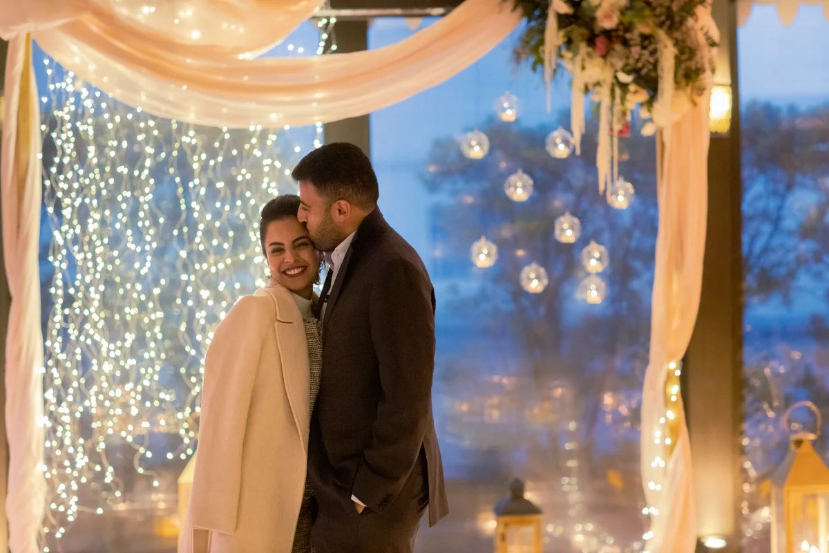 A romantic winter marriage proposal in Tuscany during the Christmas season featuring a couple celebrating under warm fairy lights, elegant draping, and glowing glass baubles