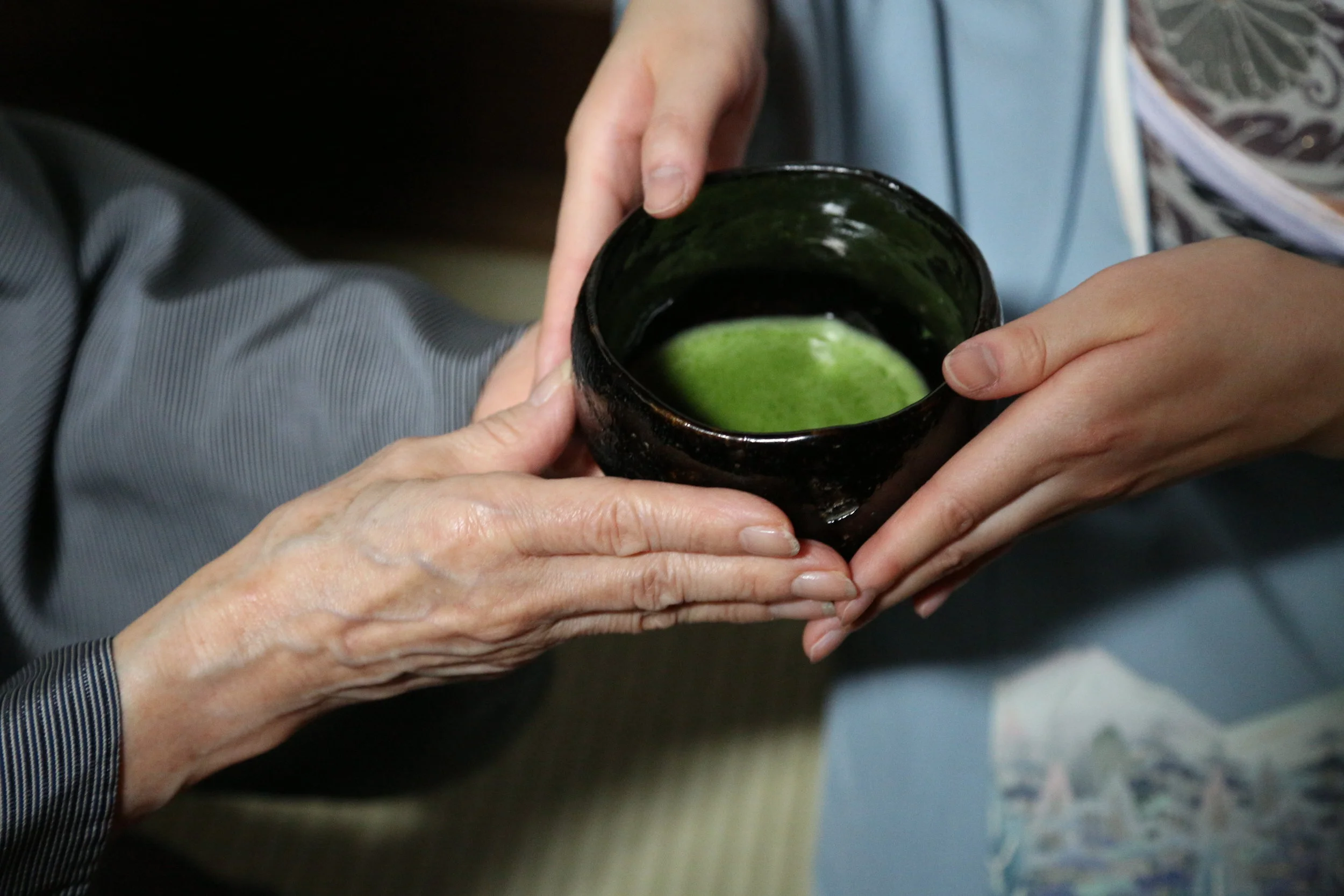 The host carefully presents the tea to the participant . ©TOKI