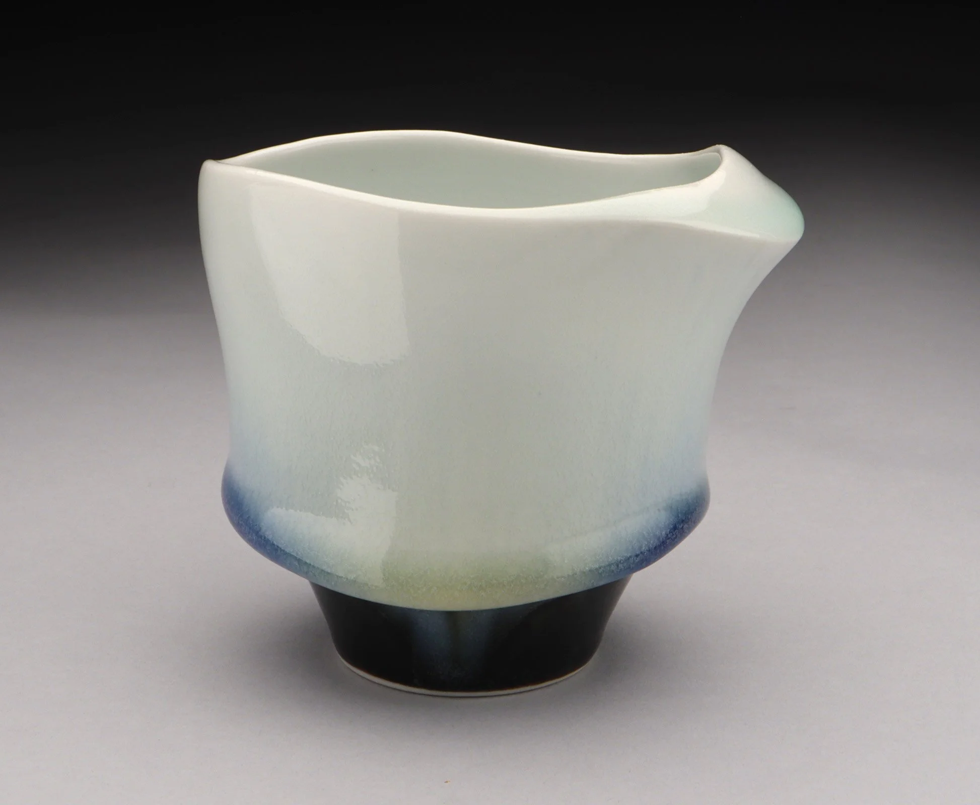 A white glazed cup, with a wide black stem. There is a ring of blue and green that is right above the stem.