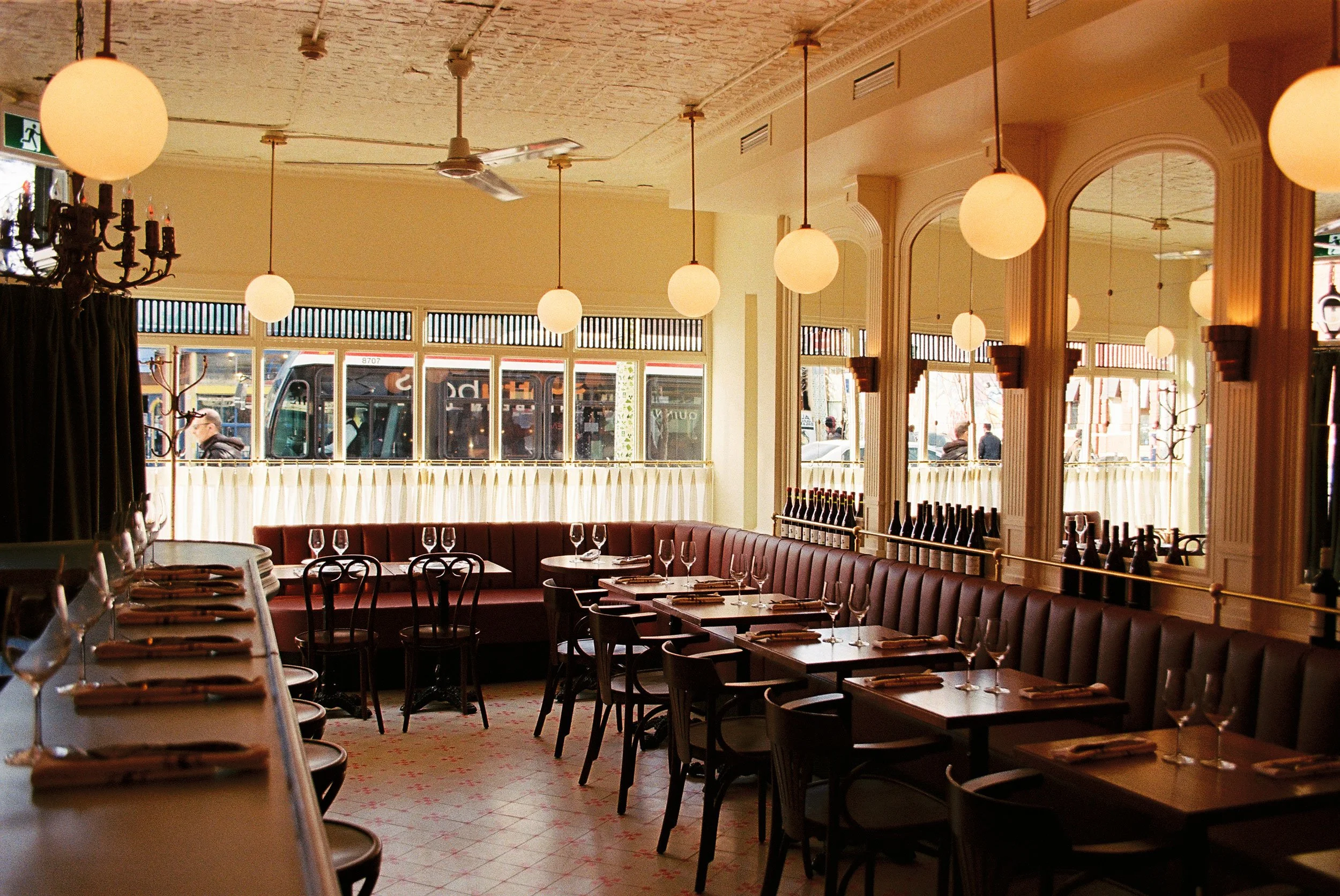 Overview of Brasserie Côte's contemporary French brasserie interior in Toronto, featuring custom millwork, a mirrored feature wall, and vintage globe lighting.