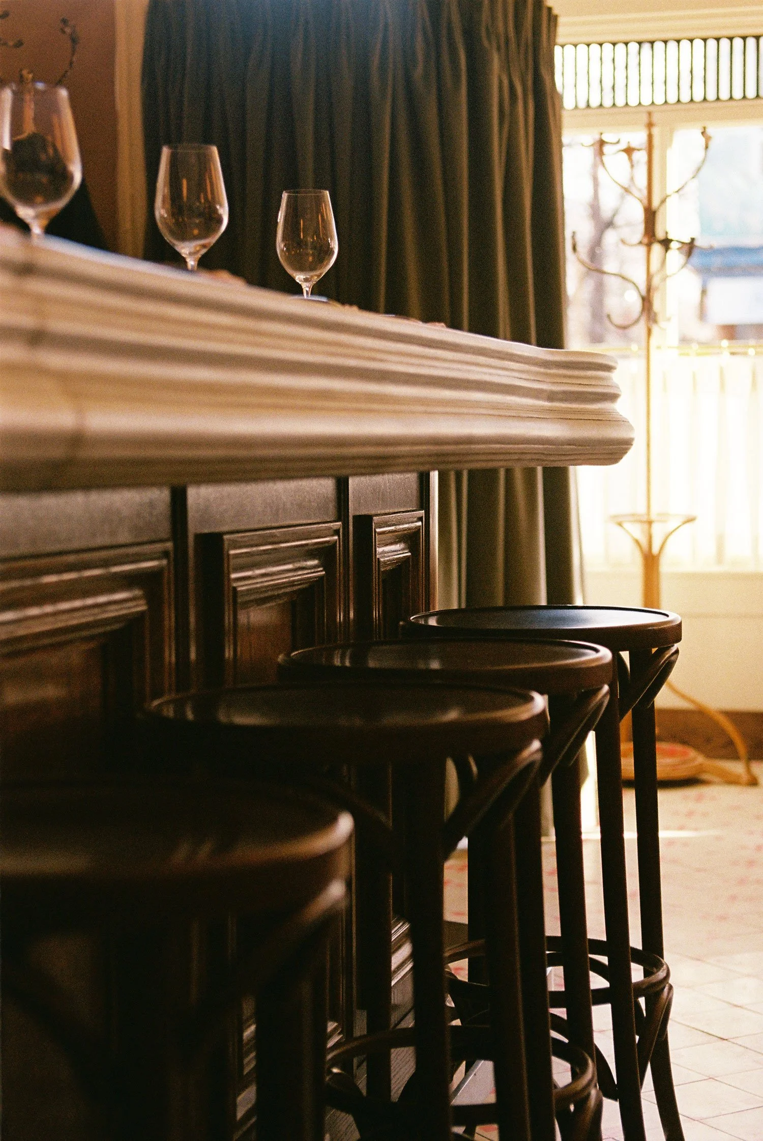 Bar stools and wine glasses at the custom bar in Brasserie Côte, a contemporary French brasserie in Toronto.