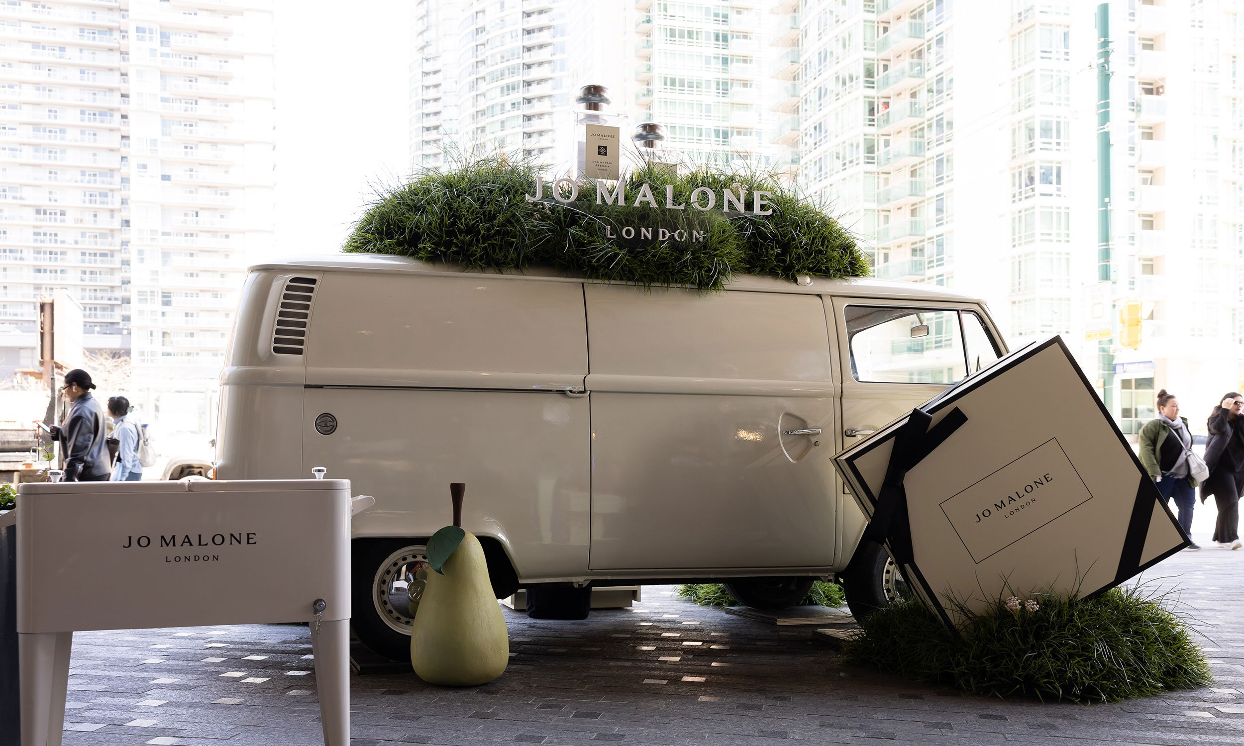 McWood's custom Jo Malone London English Pear pop-up featuring a vintage VW van with oversized grassy mounds, giant perfume bottles, flowers, and insects at The Well in Toronto.