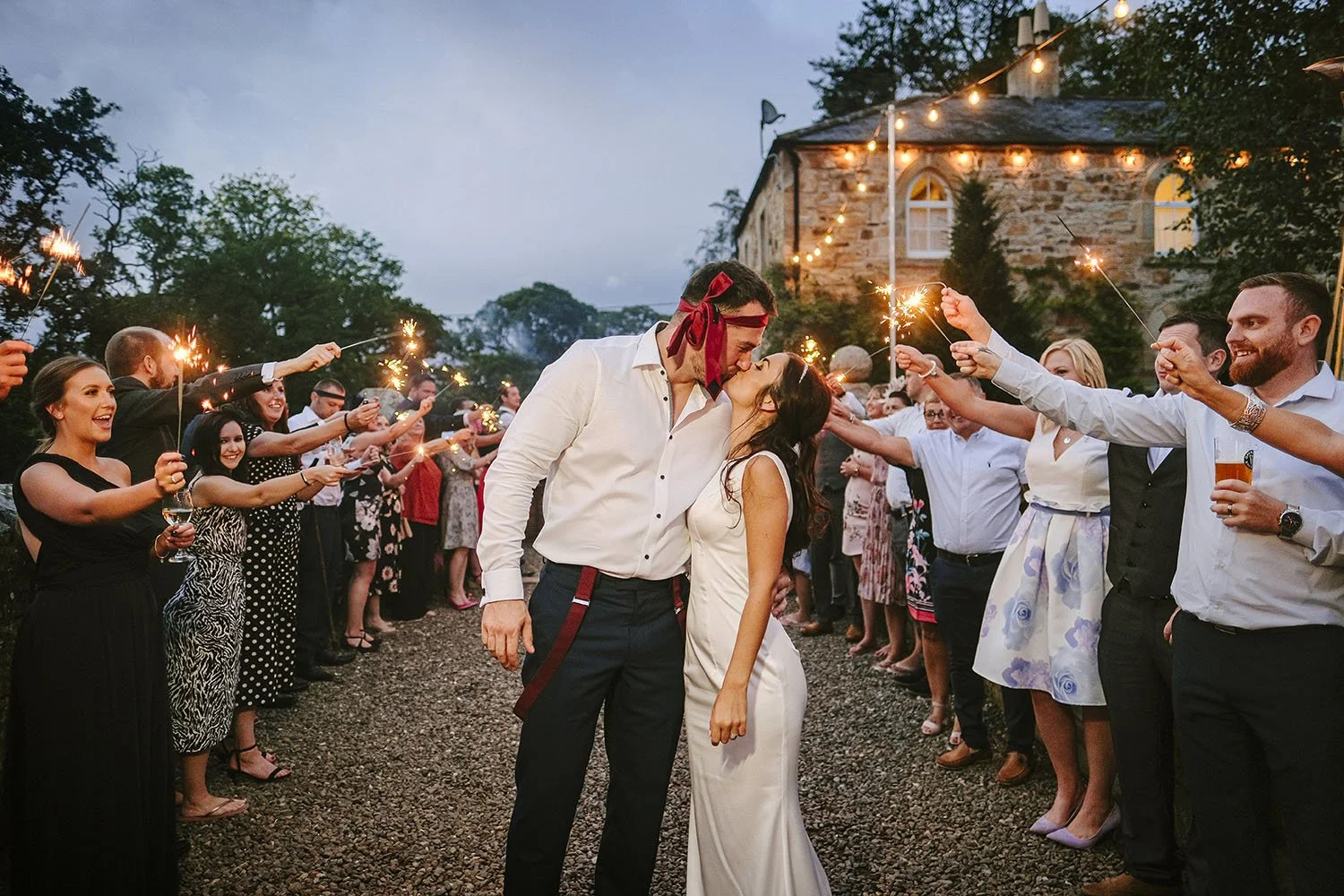 Brinkburn Priory wedding: bride and groom kissing between guests holding sparklers outside a farm venue