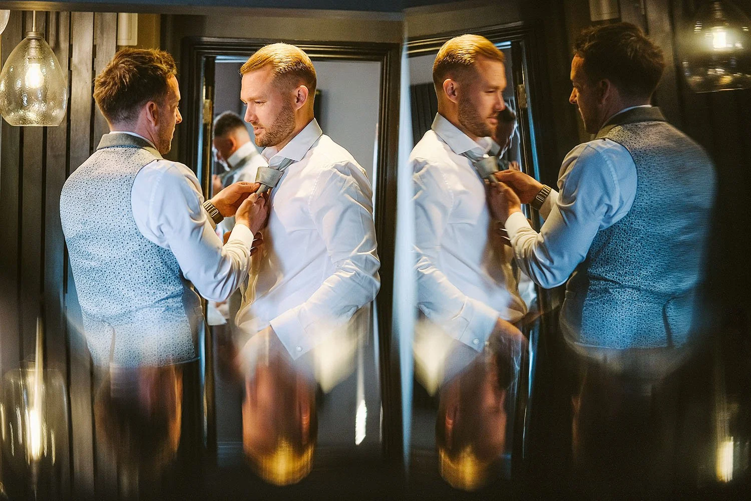 Healey Barn wedding: groomsmen in blue waistcoats adjusting each other's ties, shown in a pair of angled mirror reflections.