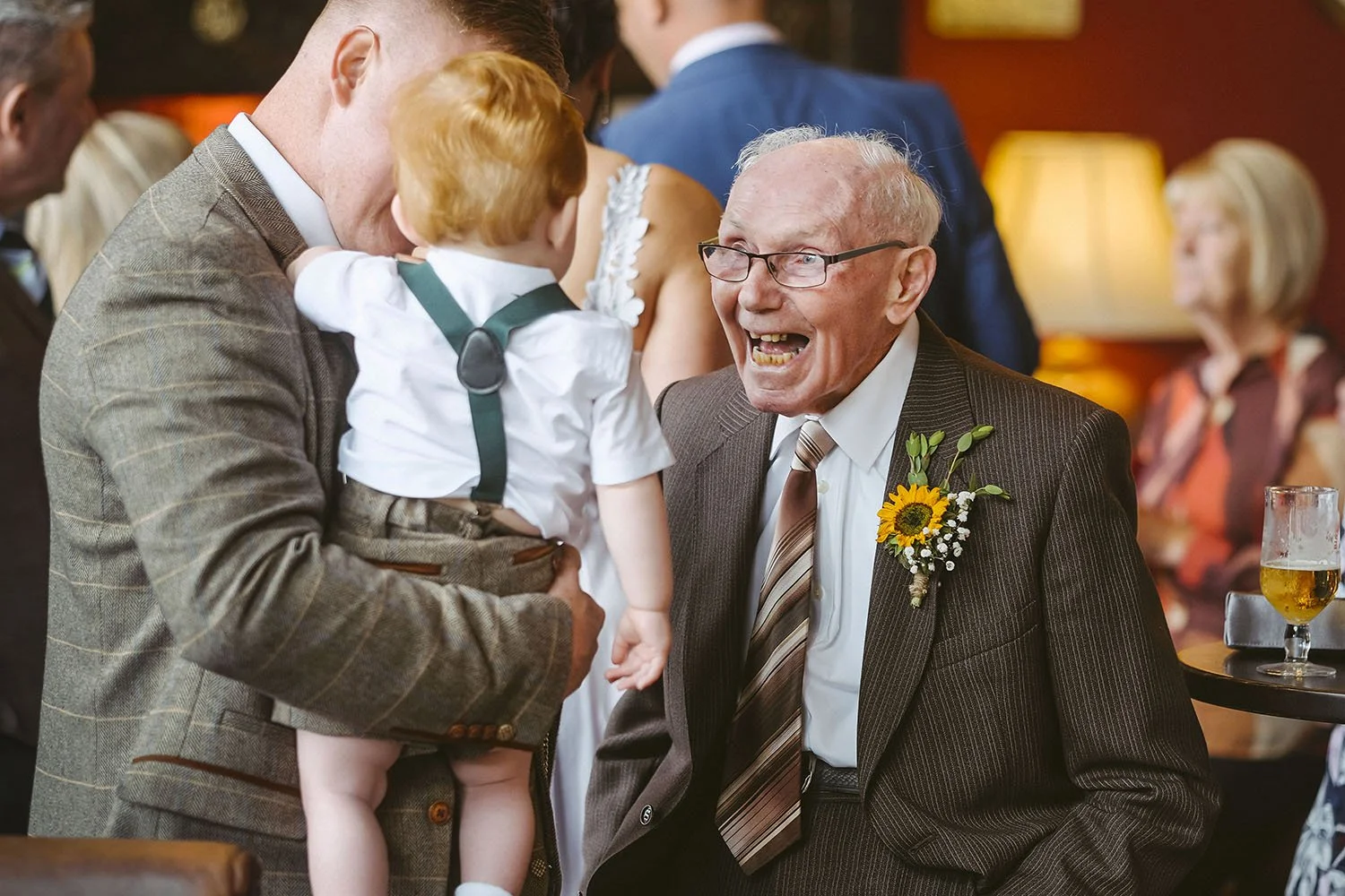 South Causey Inn wedding: elderly guest in a sunflower buttonhole laughing at a toddler held by a man at the reception.