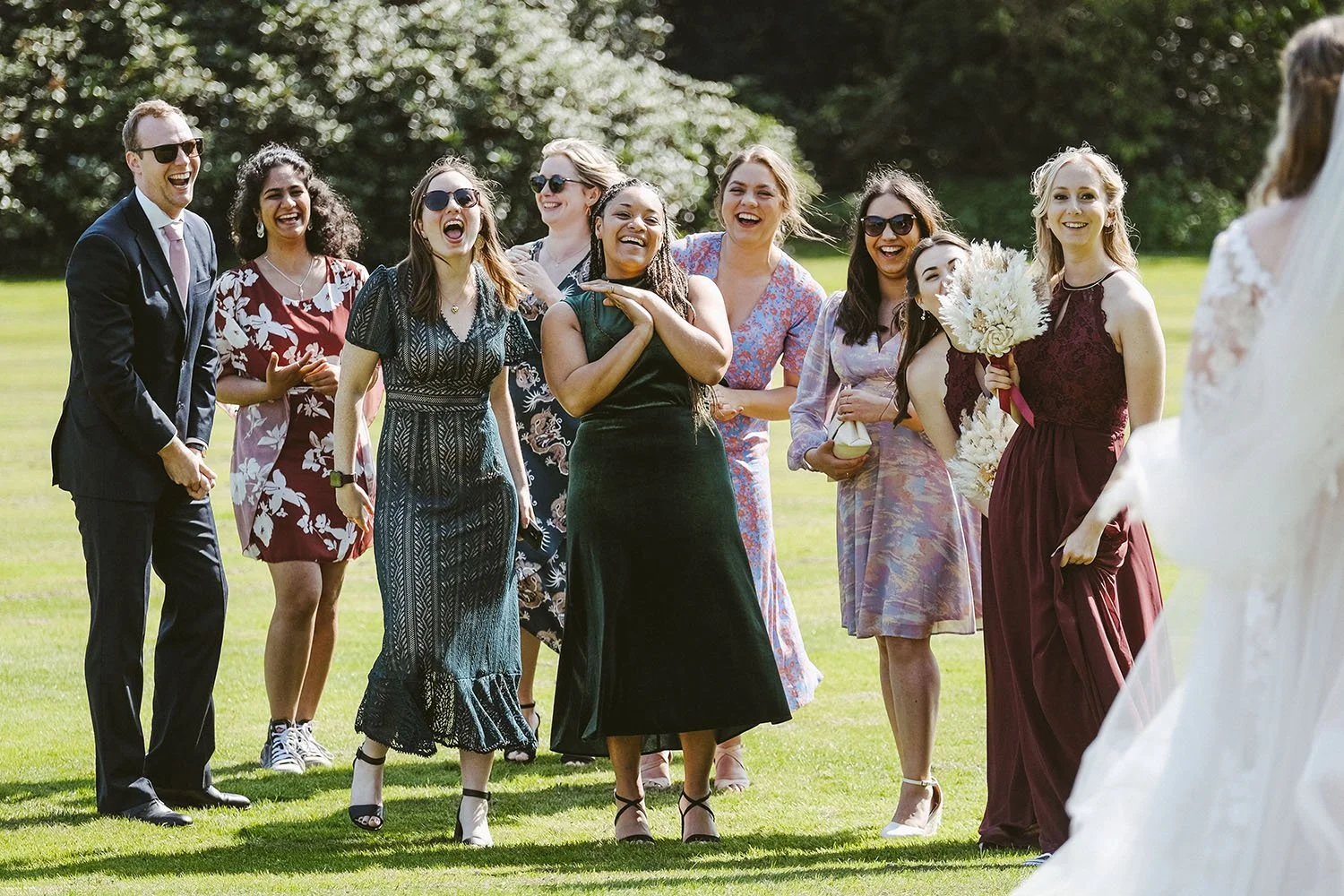Beamish Hall wedding: guests laughing together on a sunlit lawn in colourful dresses as the bride in her gown looks on.