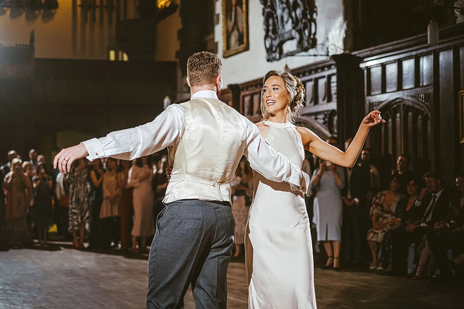 Durham Castle wedding: bride and groom dancing in a courtyard in the evening as guests watch.