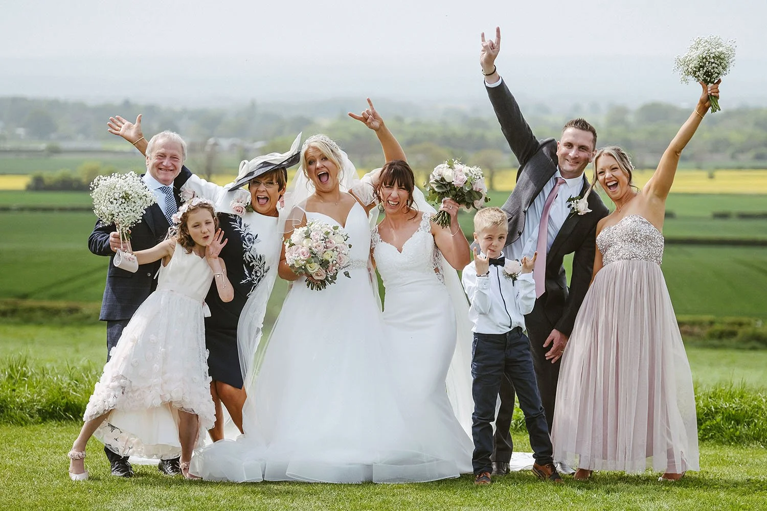 Joyful wedding party posing outdoors in a green countryside field with bouquets