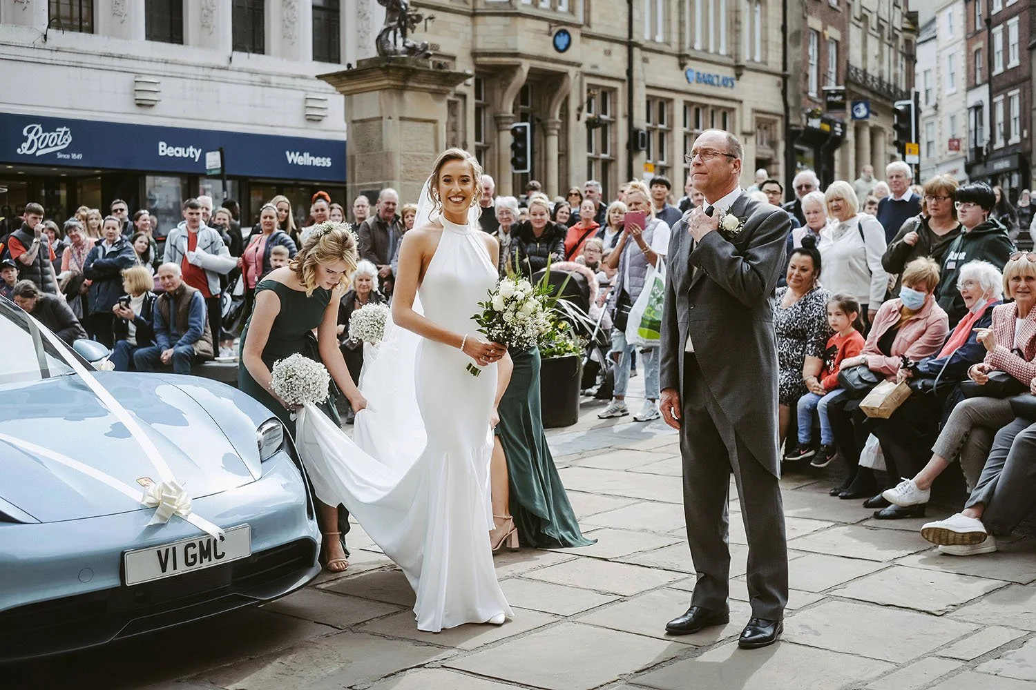 Bride and groom arriving at a city wedding in front of a cheering crowd and decorated blue sports car
