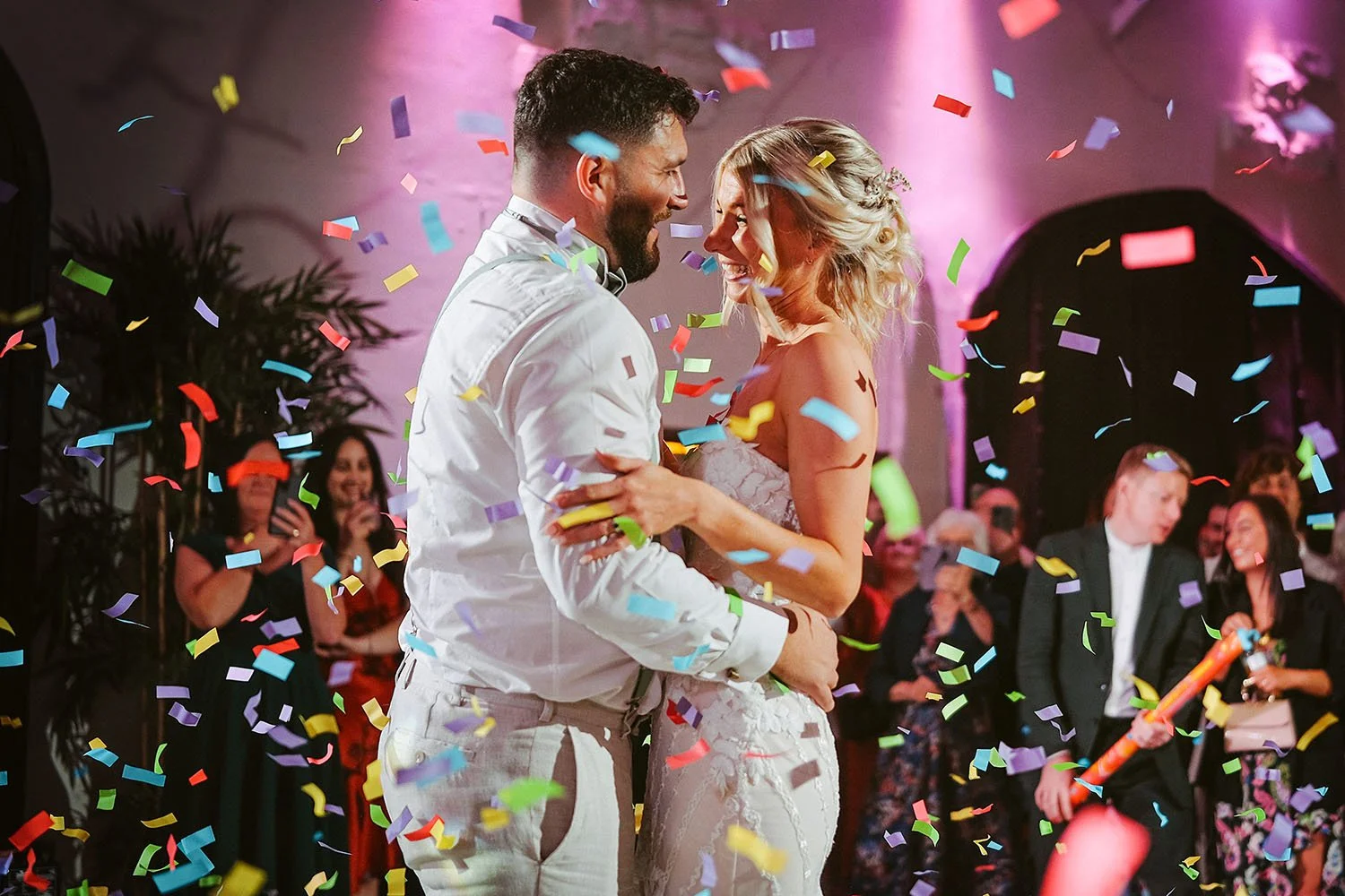 Runa Farm wedding: bride and groom dancing as colourful confetti bursts around them and guests watch in pink light.