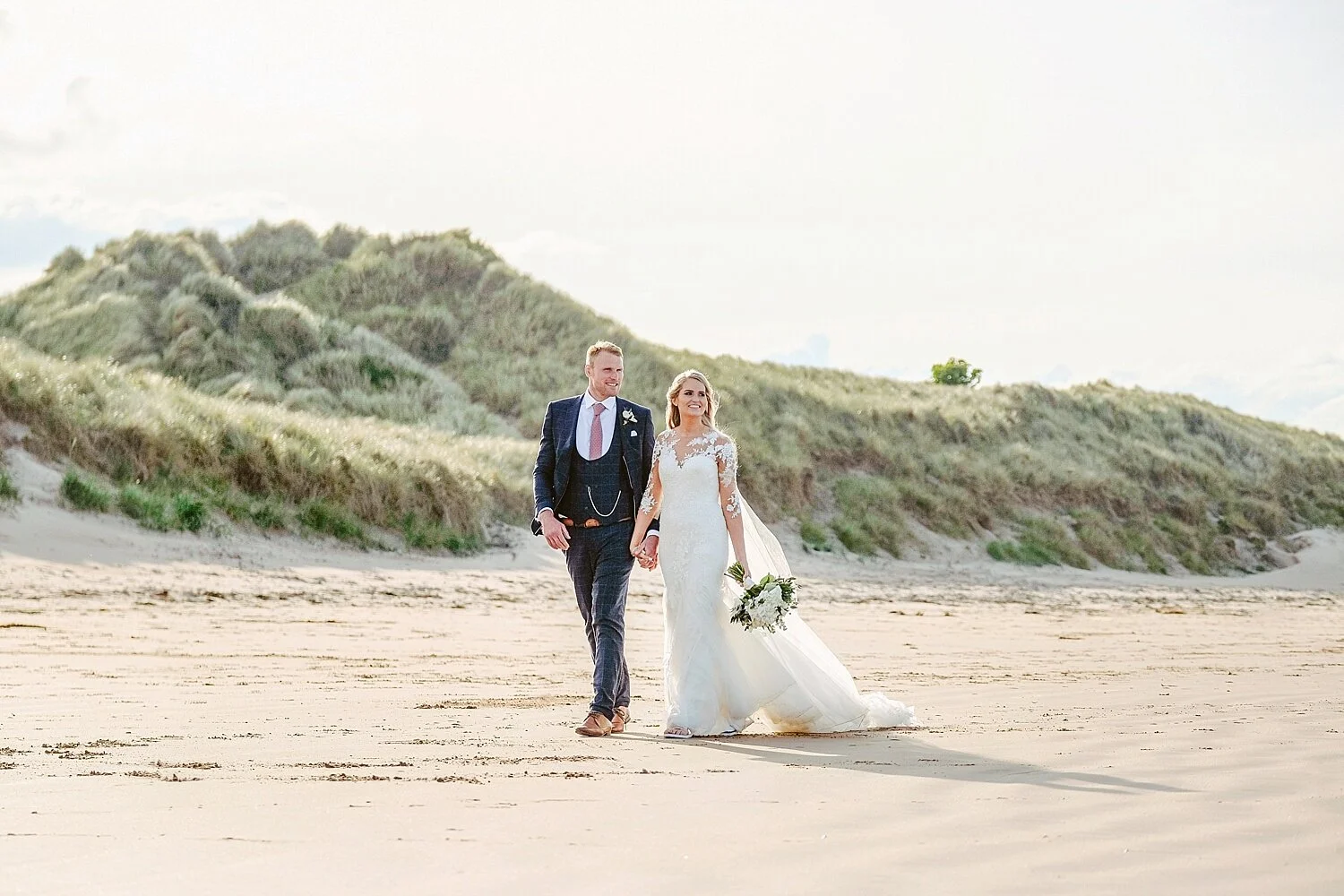 Newlyweds Georgina and Richard walking on the beach at Newton Hall