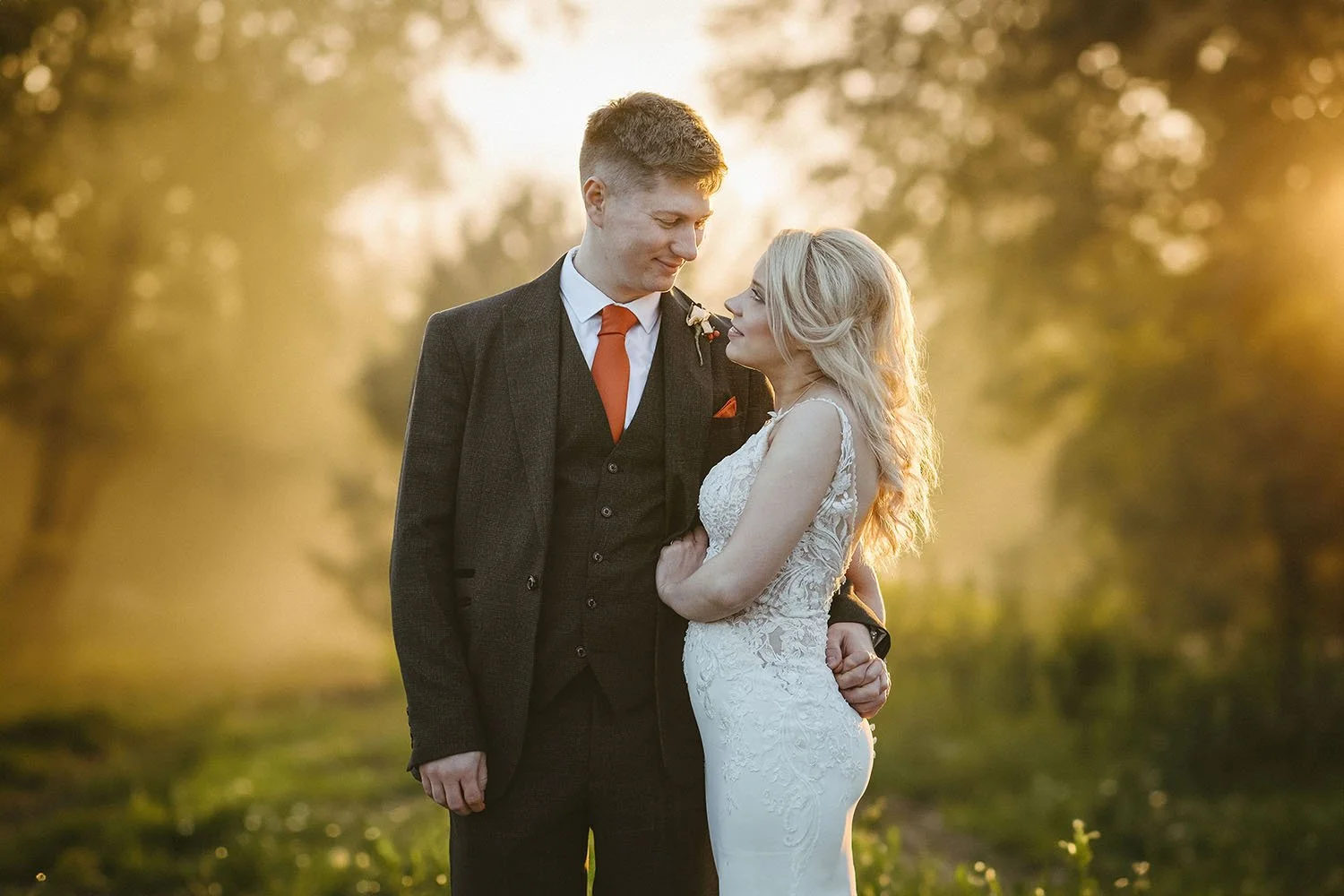 Healey Barn wedding: bride and groom embracing in a misty golden sunset glow, the groom in an orange tie.