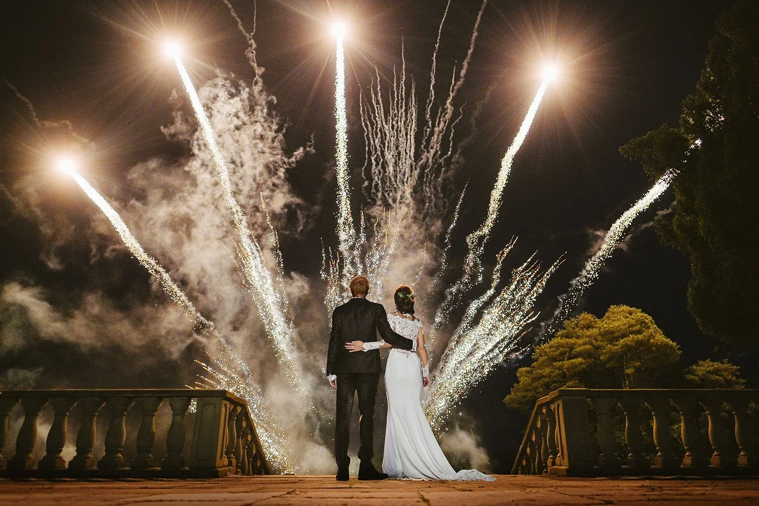 Woodhill Hall wedding: bride and groom watching fireworks shoot into the sky from a stone terrace at night