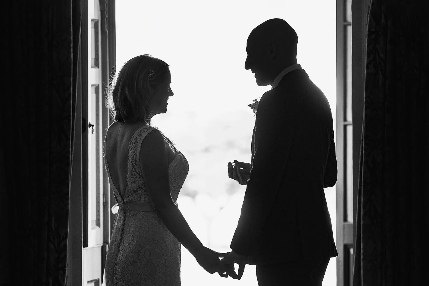Bride and groom holding hands in silhouette against a bright window