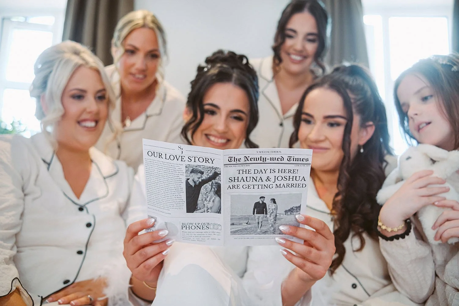 South Causey Inn wedding: bride and bridesmaids in matching pyjamas smiling as they read a keepsake newspaper together.