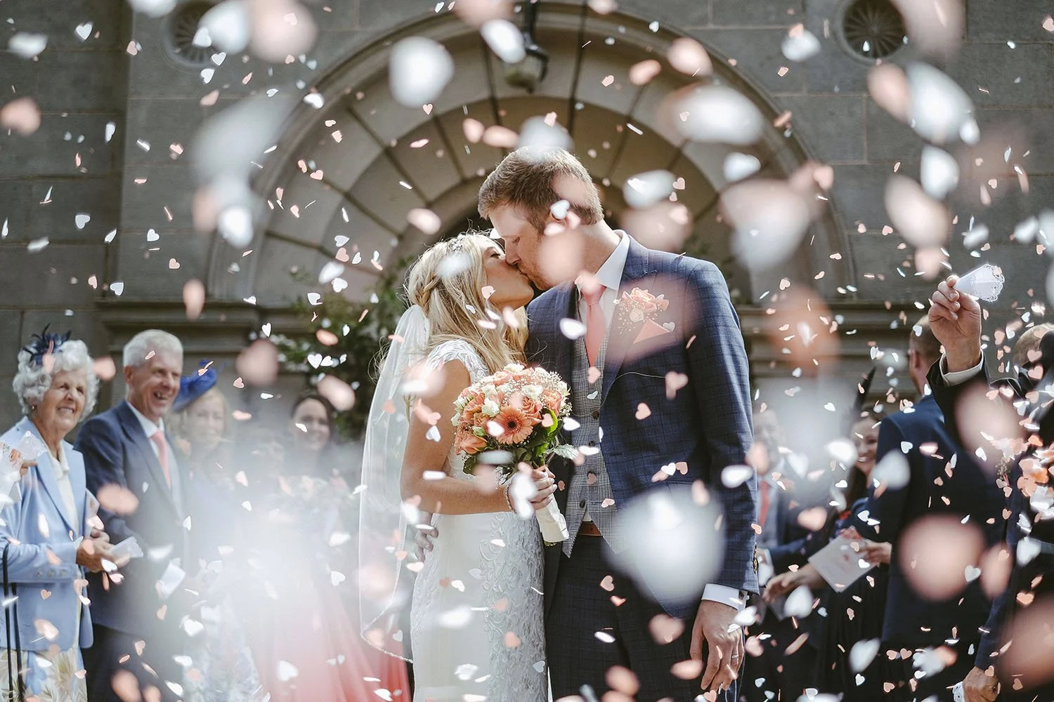 Wynyard Hall wedding: bride and groom kissing as pink petal confetti falls around them.
