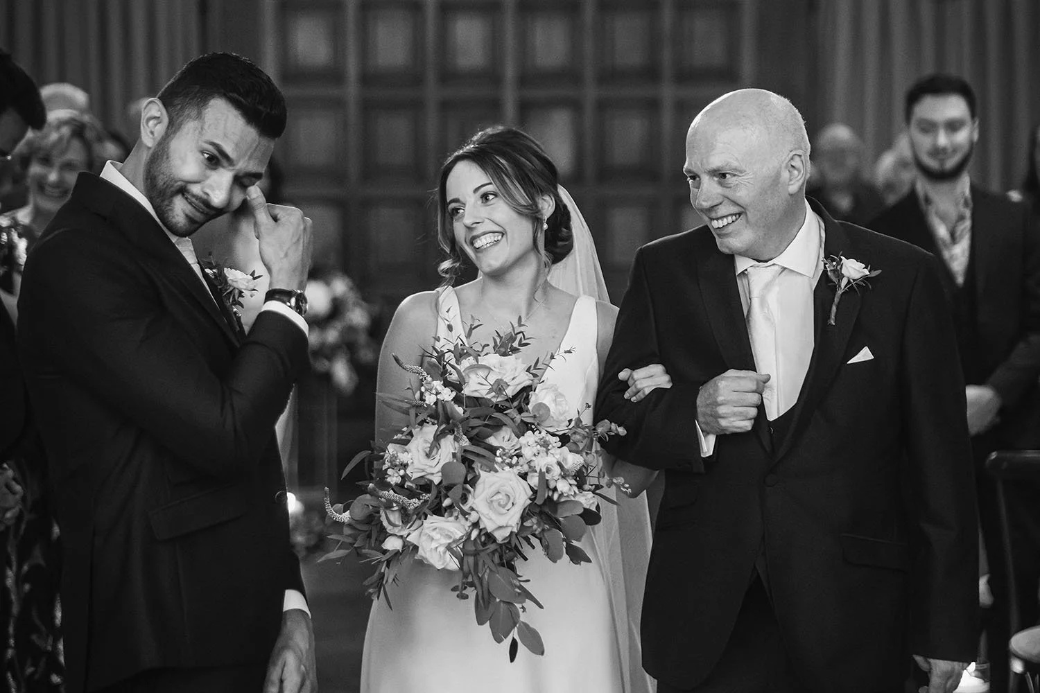 Jesmond Dene House wedding: groom wiping away a tear as the bride arrives on her father's arm, in black and white.