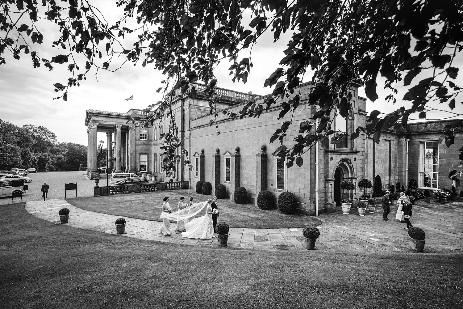 Wynyard Hall wedding: wide view of the bride and bridesmaids arriving in front of a country house, black and white