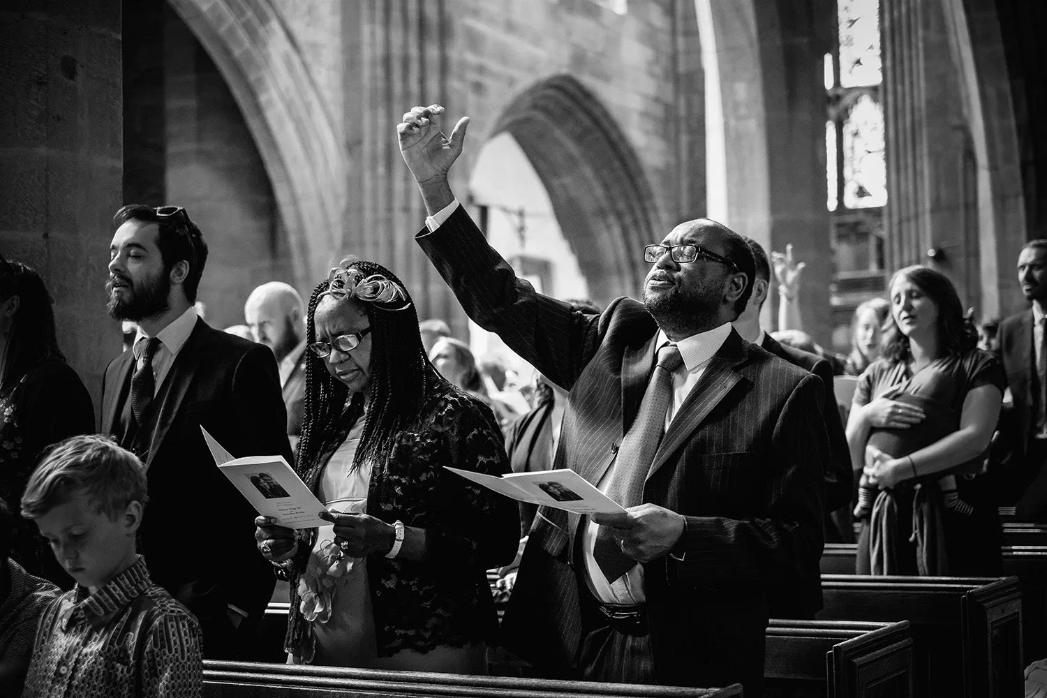 Church wedding guests singing hymns, one man raising his arm, black and white