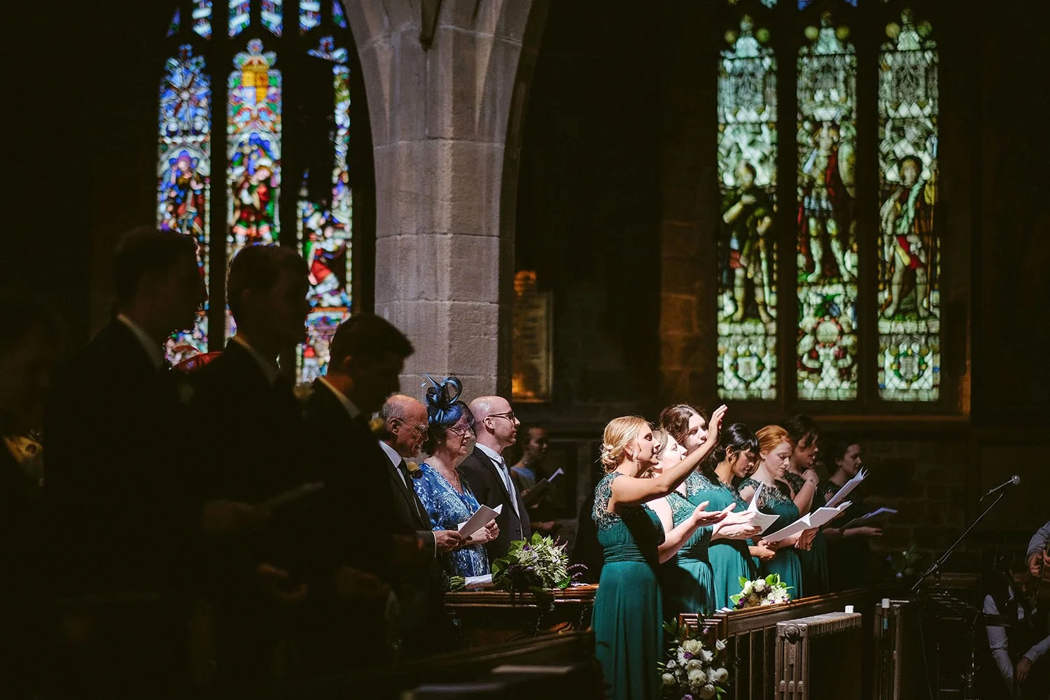 Choir singing in a church wedding with stained glass windows behind them