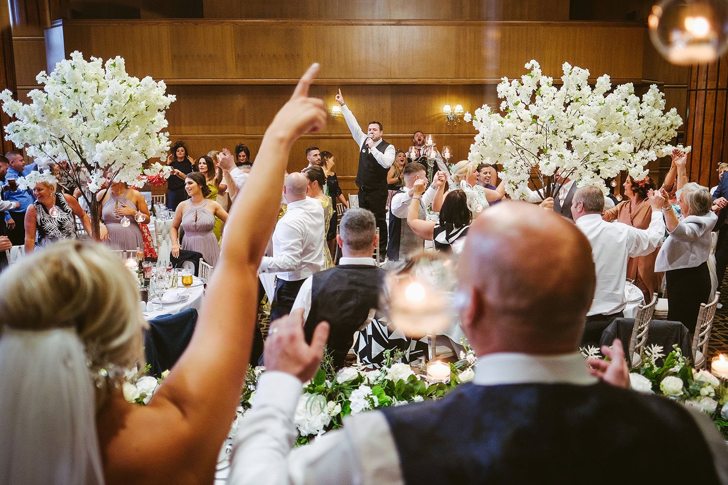 The Vermont Hotel wedding: bride and guests cheering with raised arms among white blossom trees at the wedding breakfast