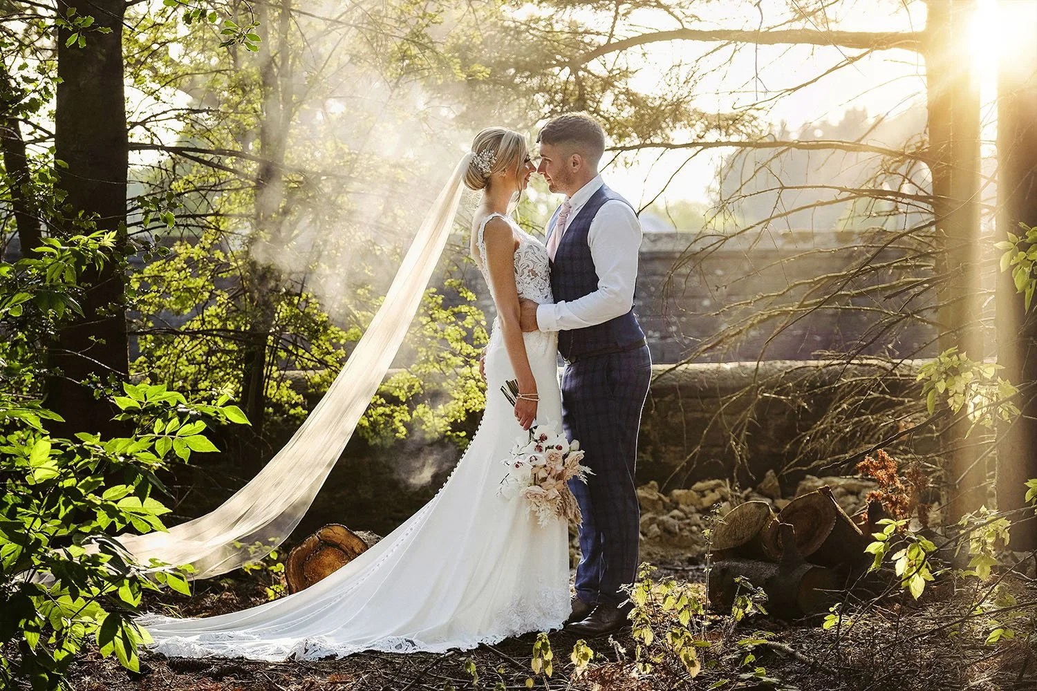 Shotton Grange wedding: bride and groom nose to nose in a sunlit woodland, her long veil trailing behind.