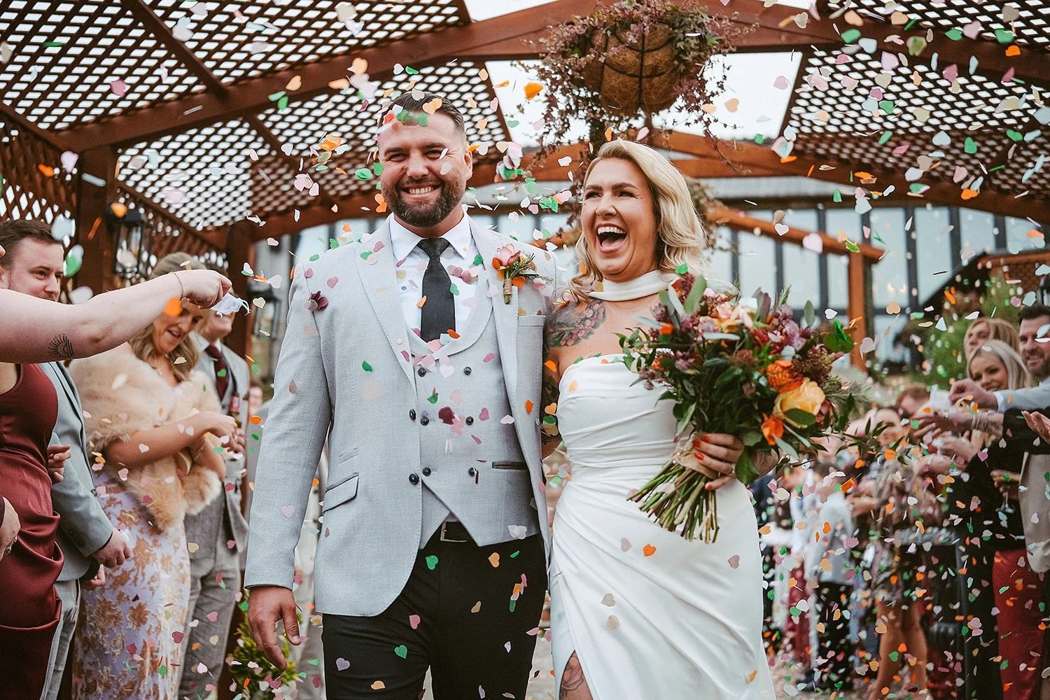 South Causey Inn wedding: bride and groom laughing as colourful confetti falls under a wooden pergola